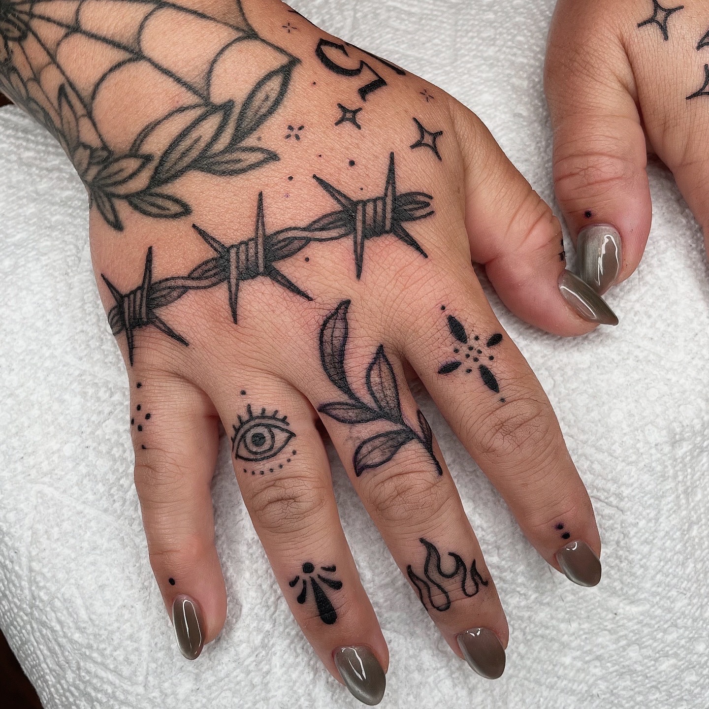 Barbed wire and floral black and grey tattoo on the hand by Emily Lux