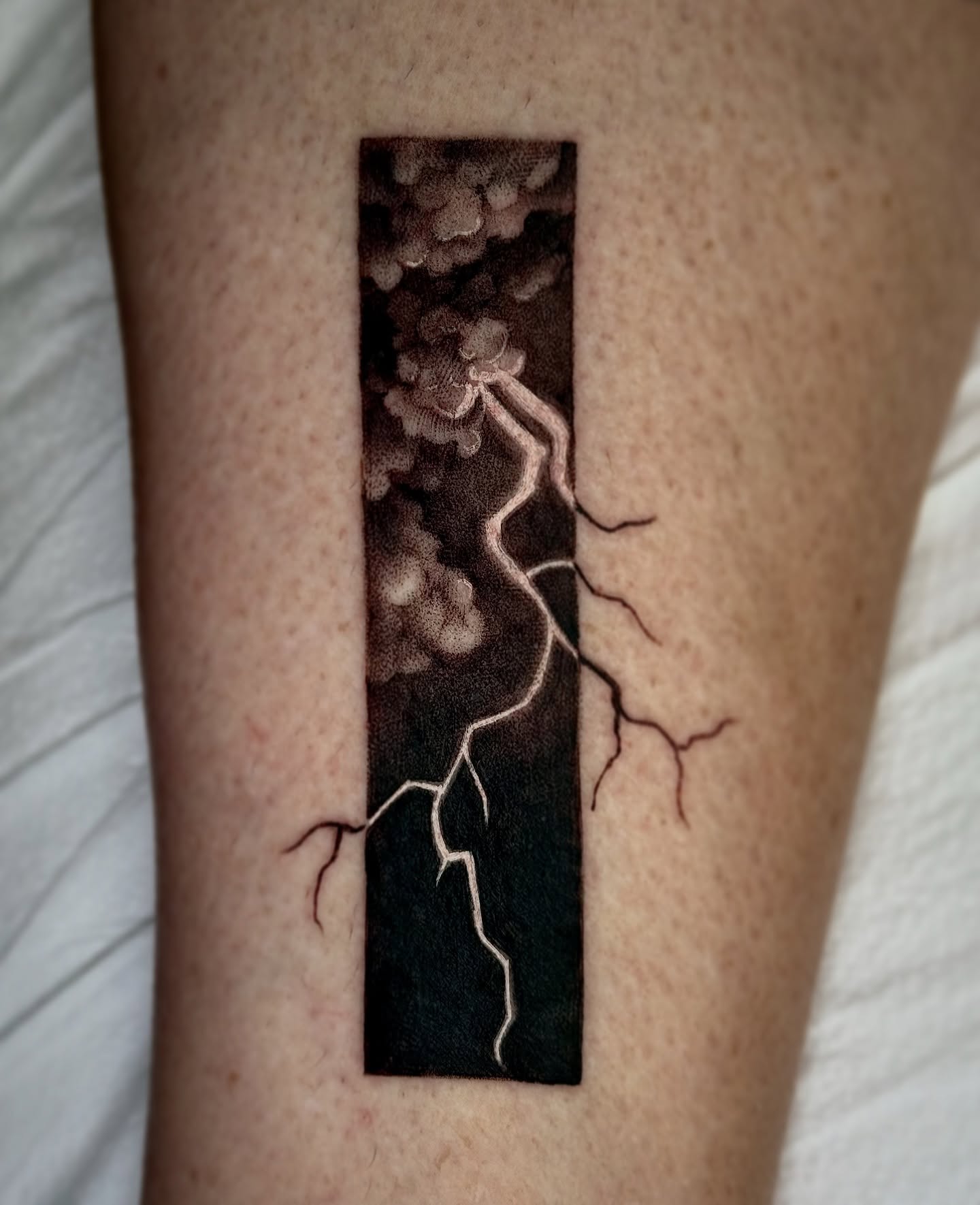 Lightning and clouds black and grey tattoo on the forearm by Lydia Jude
