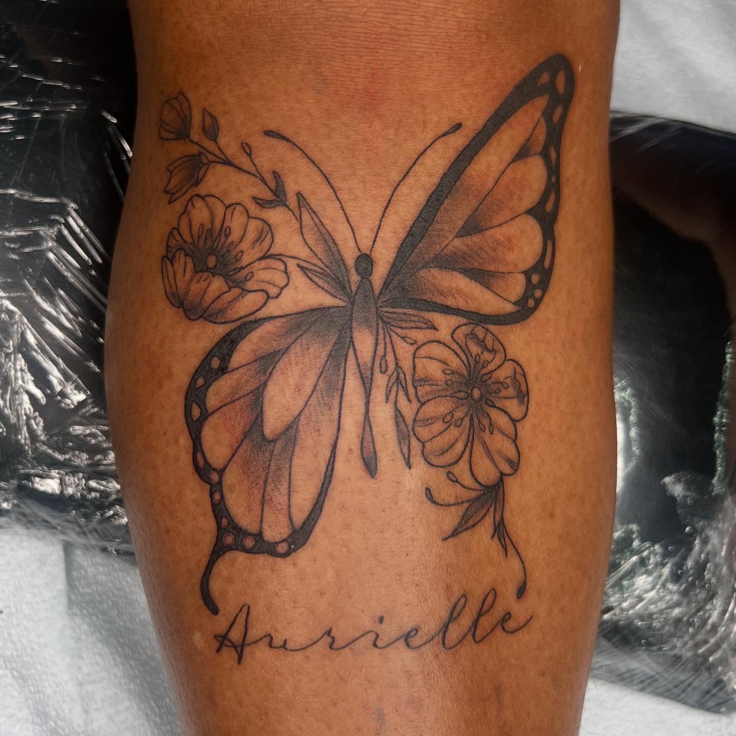 Butterfly and flowers black and grey tattoo on the thigh by Monii Arreola