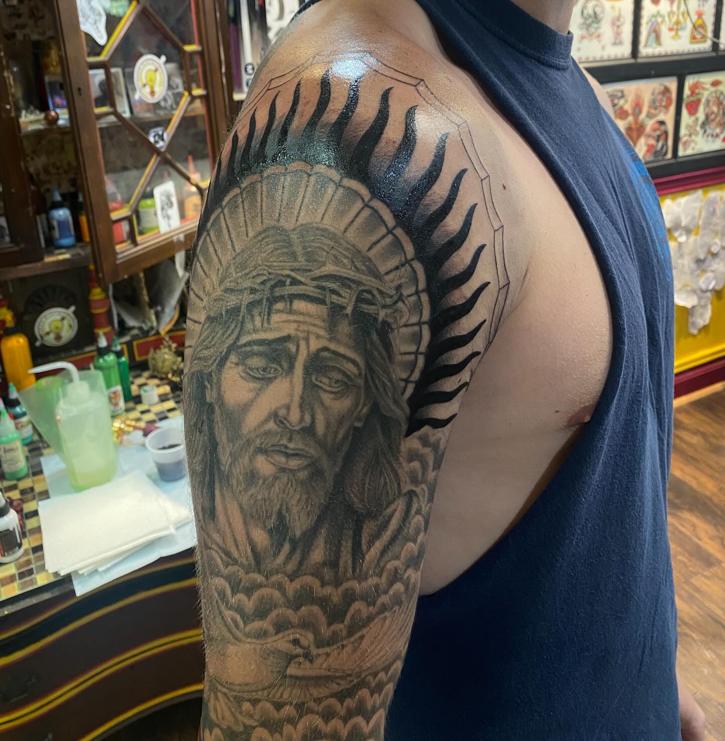 Religious figure black and grey tattoo on the upper arm by Thomas Cook