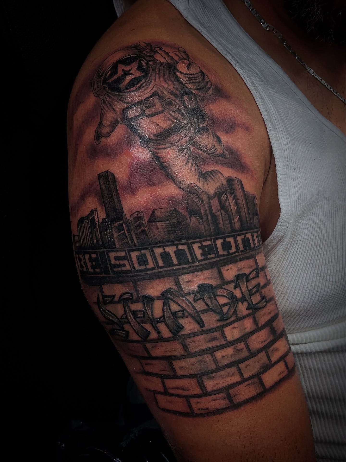 Astronaut and cityscape realism tattoo on the upper arm by Christa Martinez