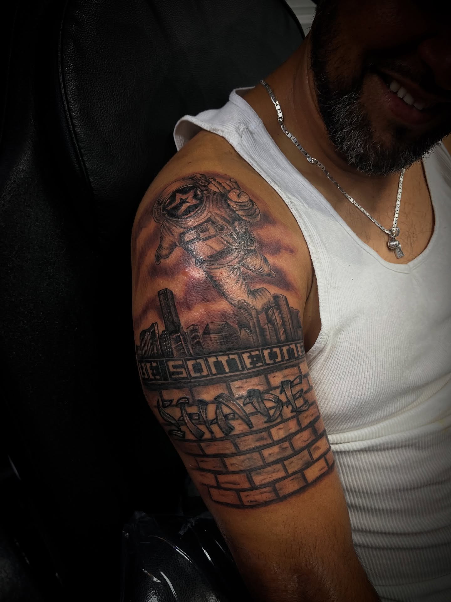 Cityscape with astronaut realism tattoo on the upper arm by Christa Martinez