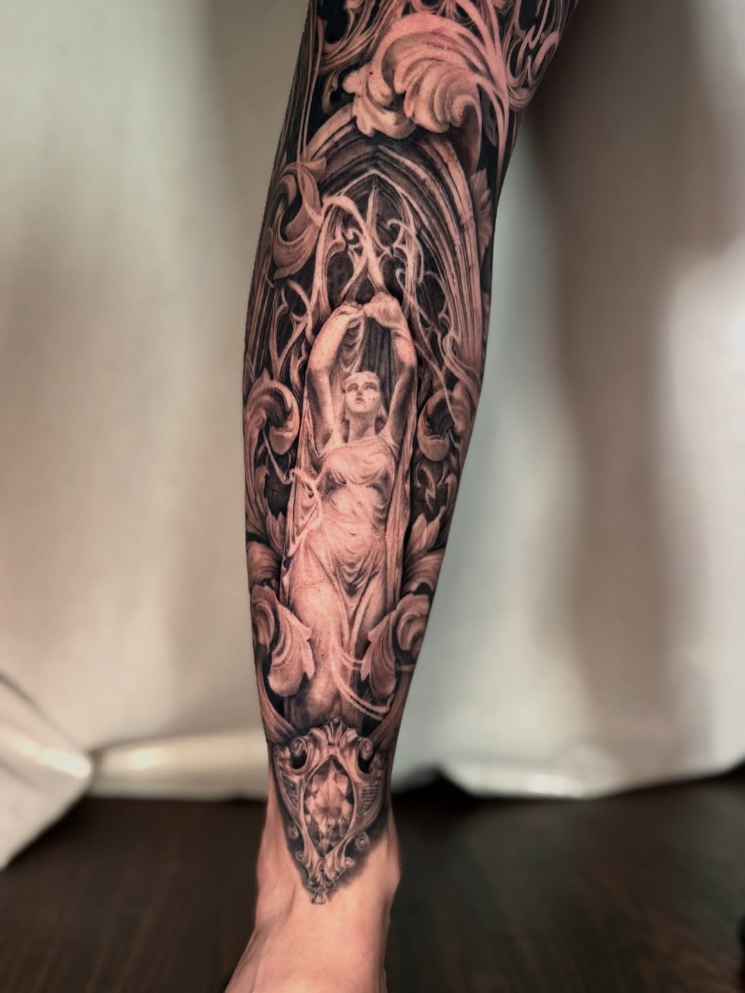Statue with ornate frame realism tattoo on the forearm by April Lynn