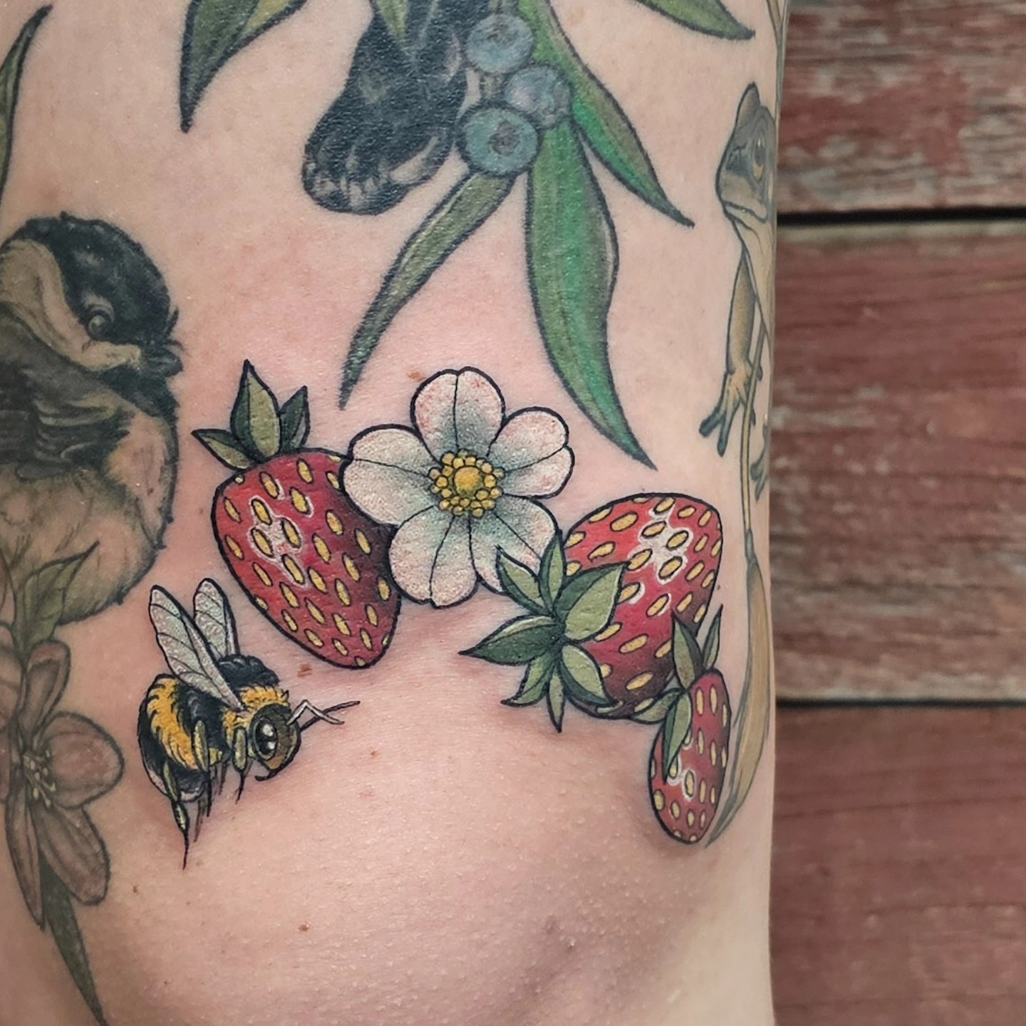 Strawberries, flowers, bee American traditional tattoo on the upper arm by Savannah