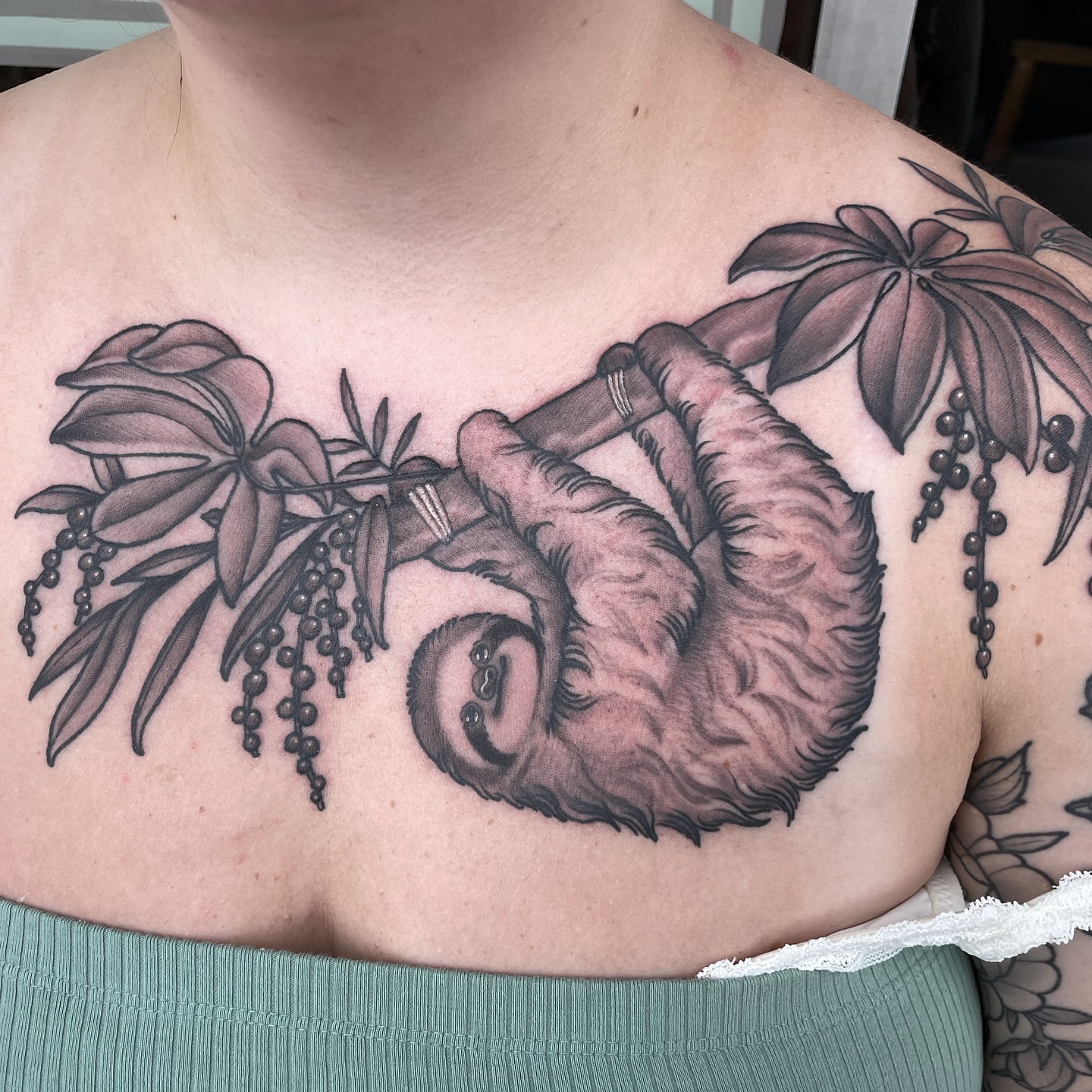 Sloth and foliage realism tattoo on the chest by Emily Lux