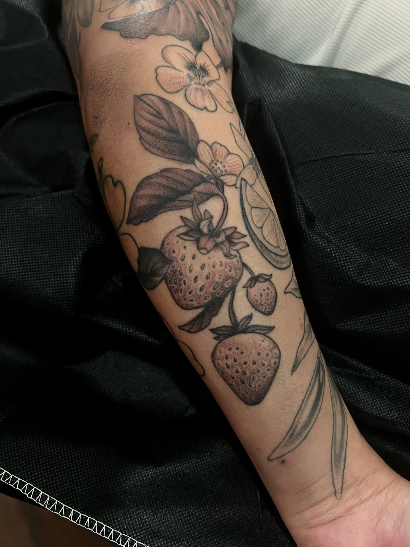 Strawberries and flowers black and grey tattoo on the forearm by Avrey Simone