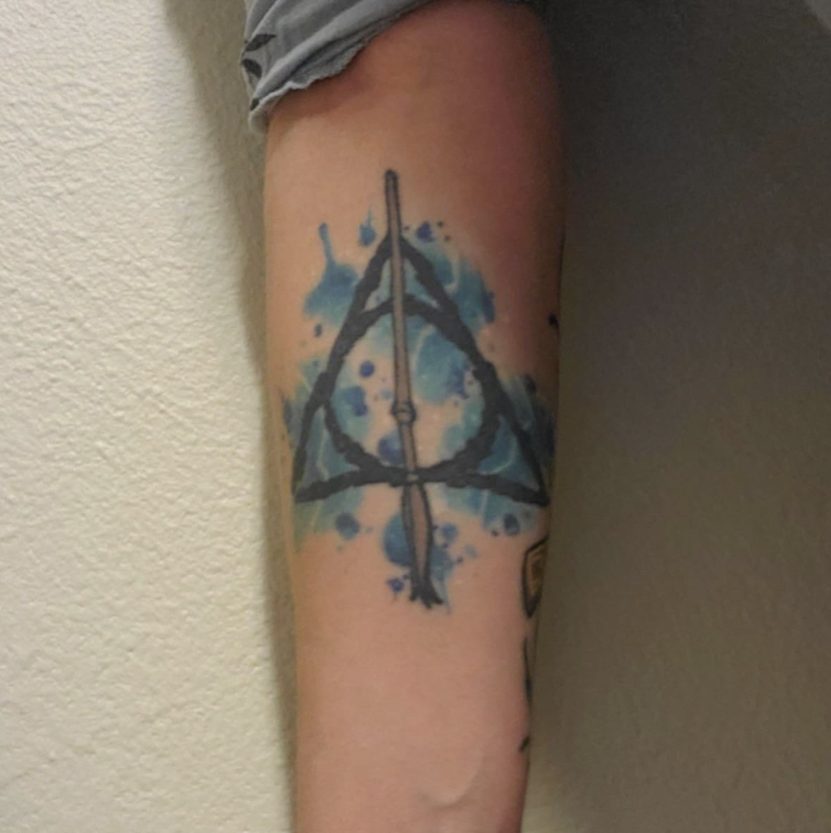 Deathly hallows symbol watercolor tattoo on the forearm by Savannah Compton