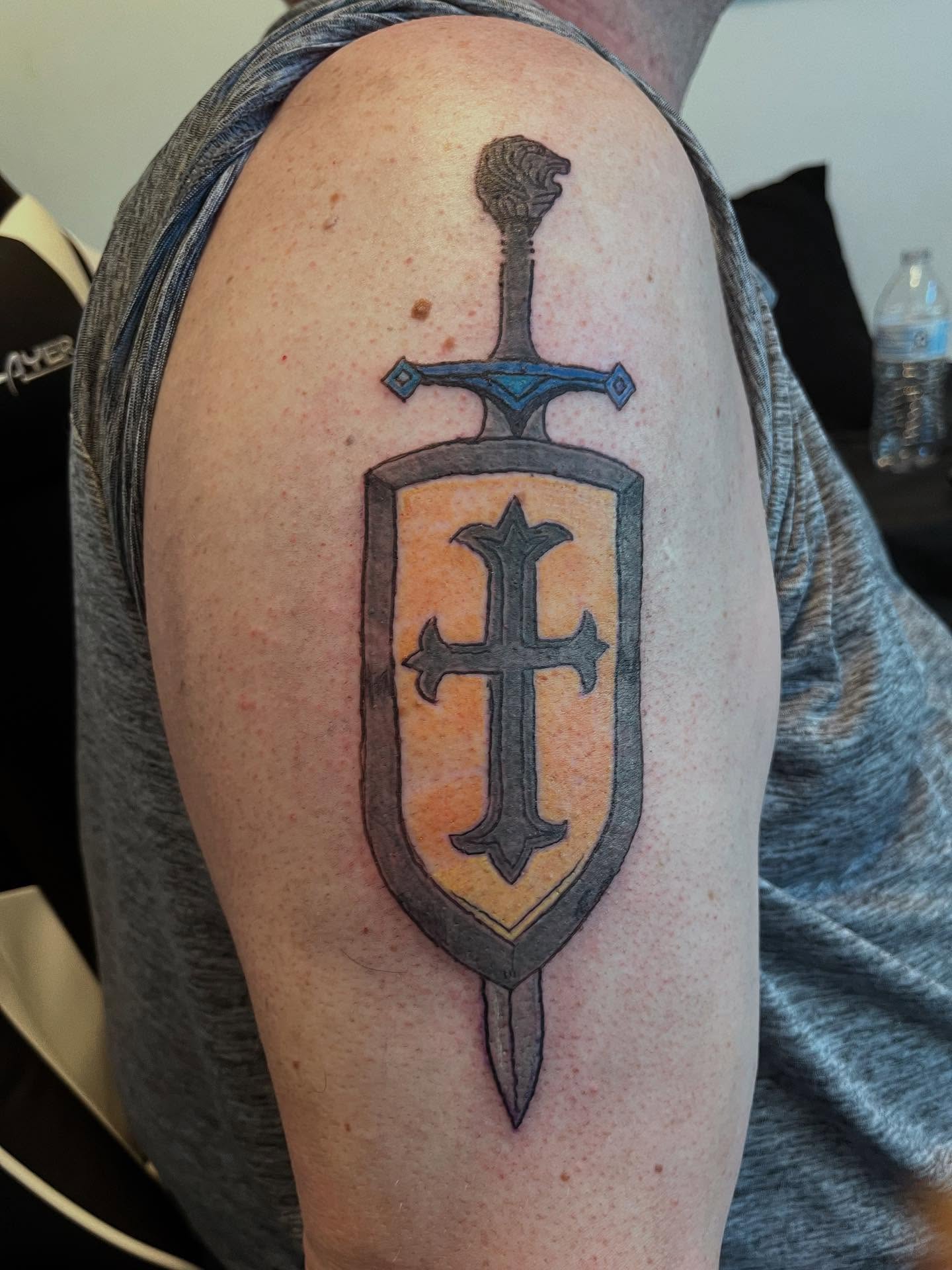 Sword and shield black and grey tattoo on the shoulder by Val Maughan