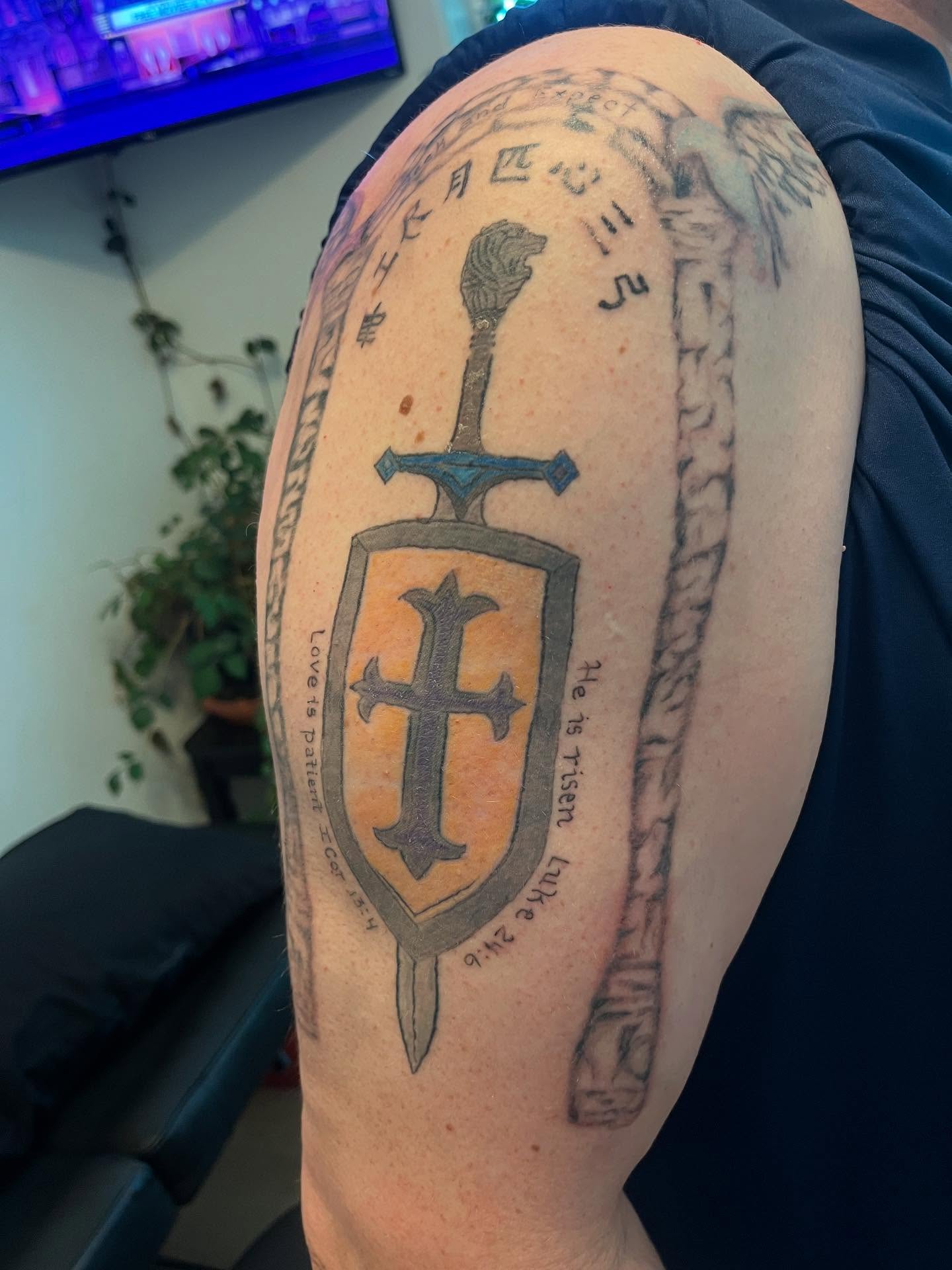 Sword and shield black and grey tattoo on the upper arm by Val Maughan
