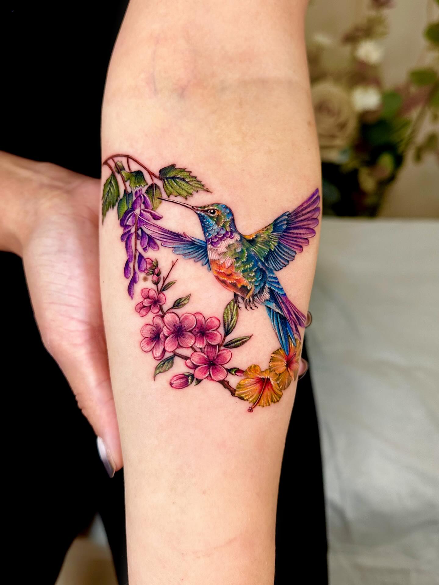 Hummingbird and flowers watercolor tattoo on the forearm by Claire