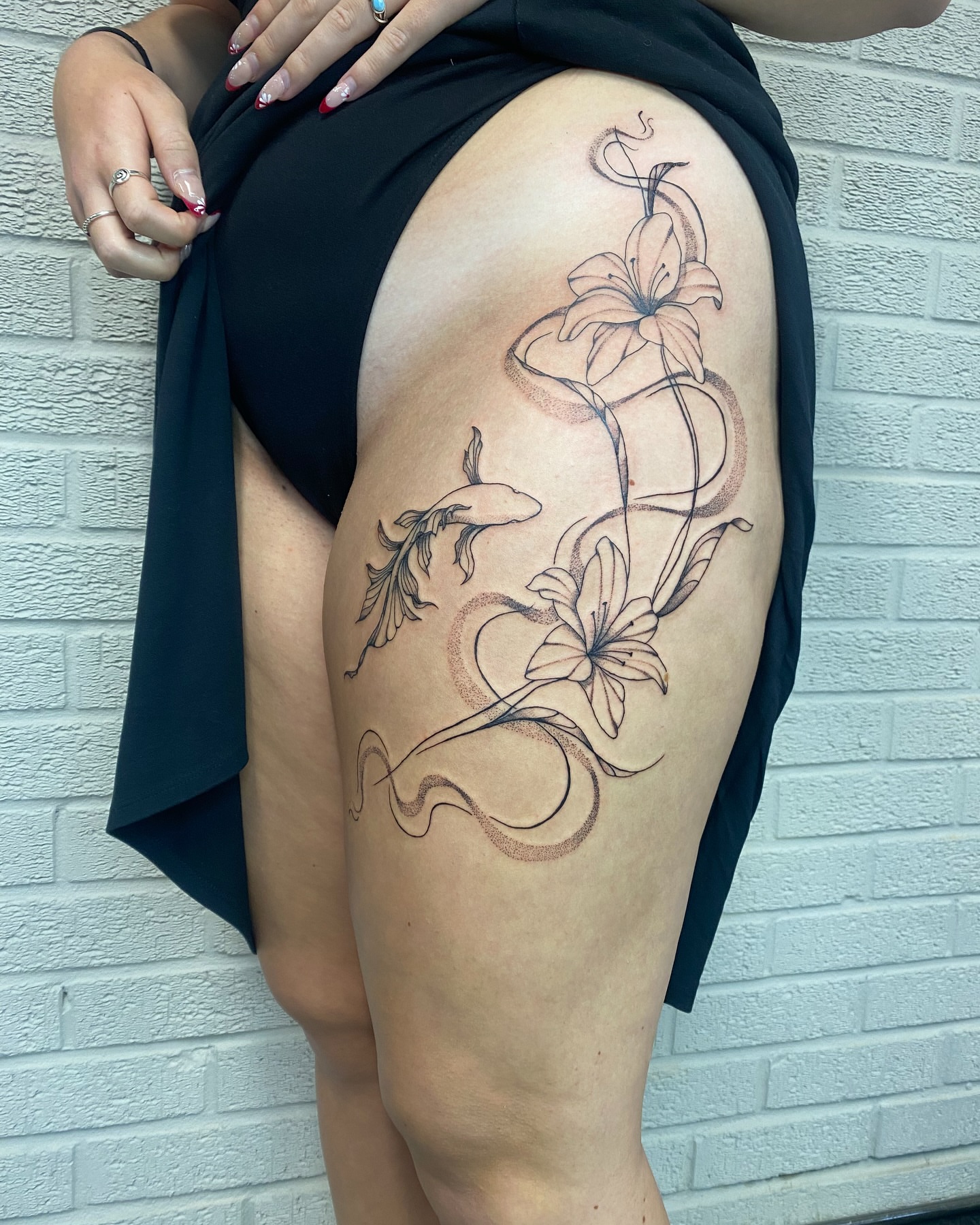 Lilies and fish black and grey tattoo on the thigh by Ellena Reggiani