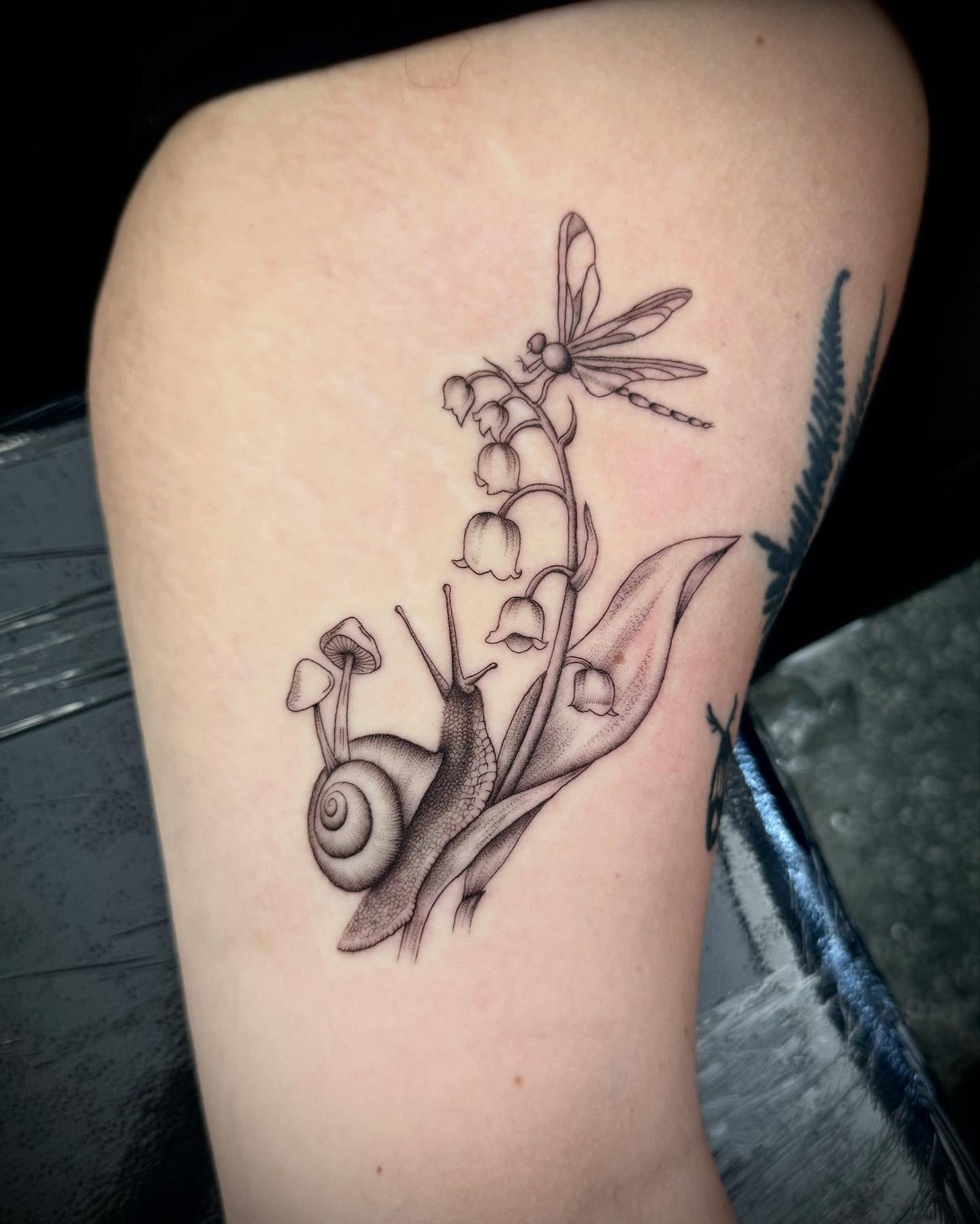 Snail and lilies of the valley realism tattoo on the forearm by oh hey, robin.
