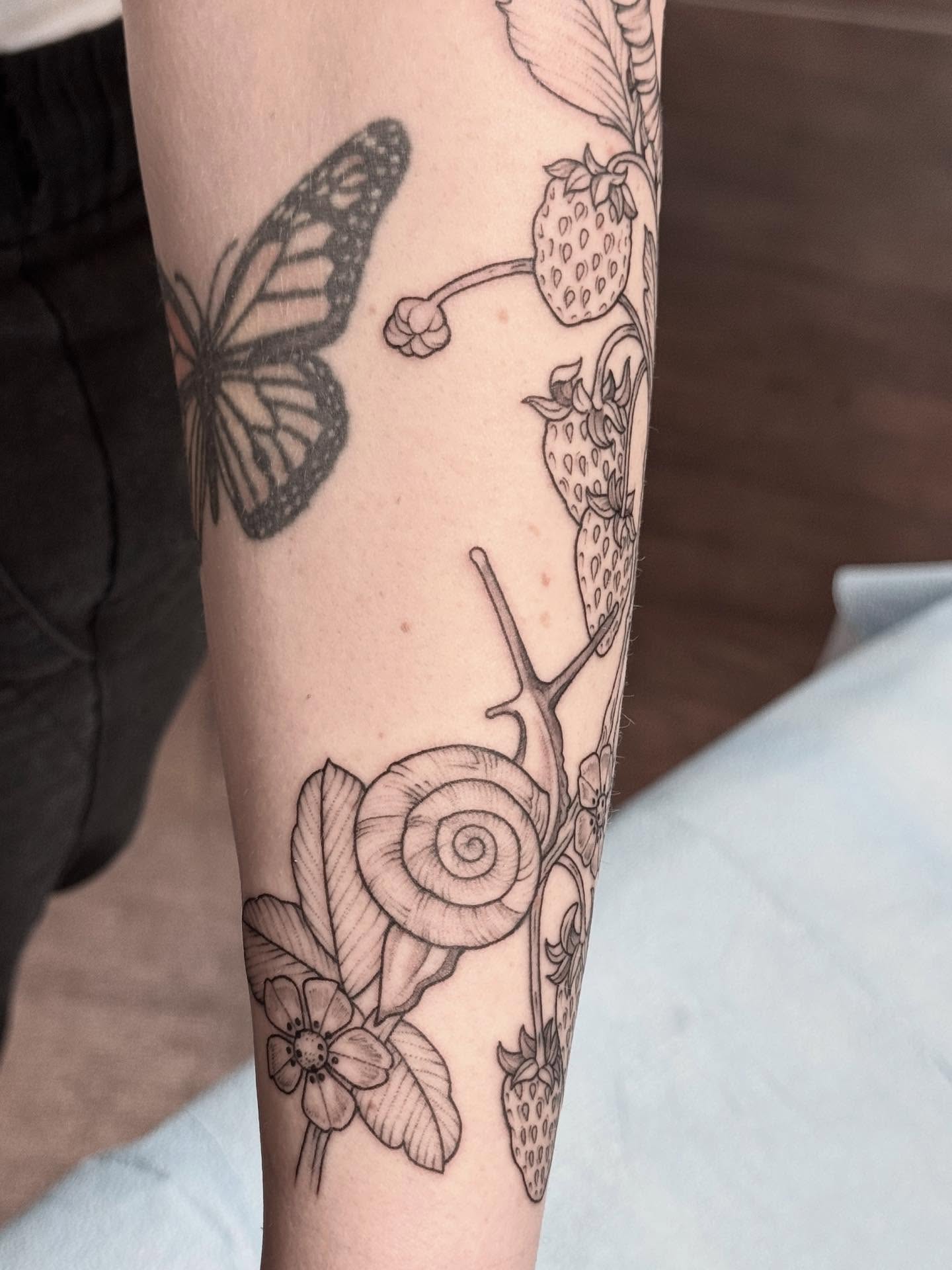 Butterfly, strawberries, snail, flowers black and grey tattoo on the forearm by Kirsten Marsden Ballantyne
