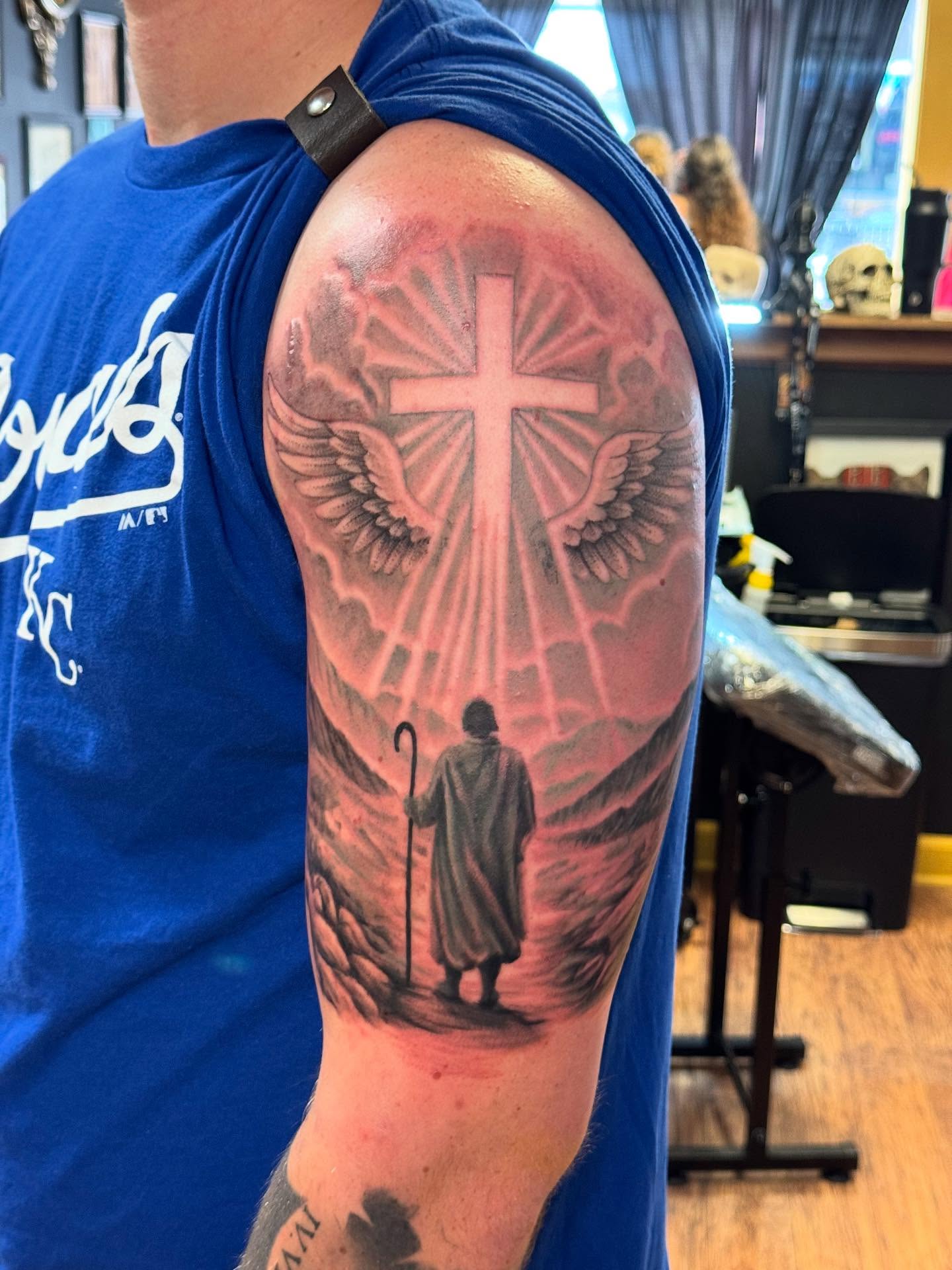 Cross with wings realism tattoo on the upper arm by Kyle J. Bishop