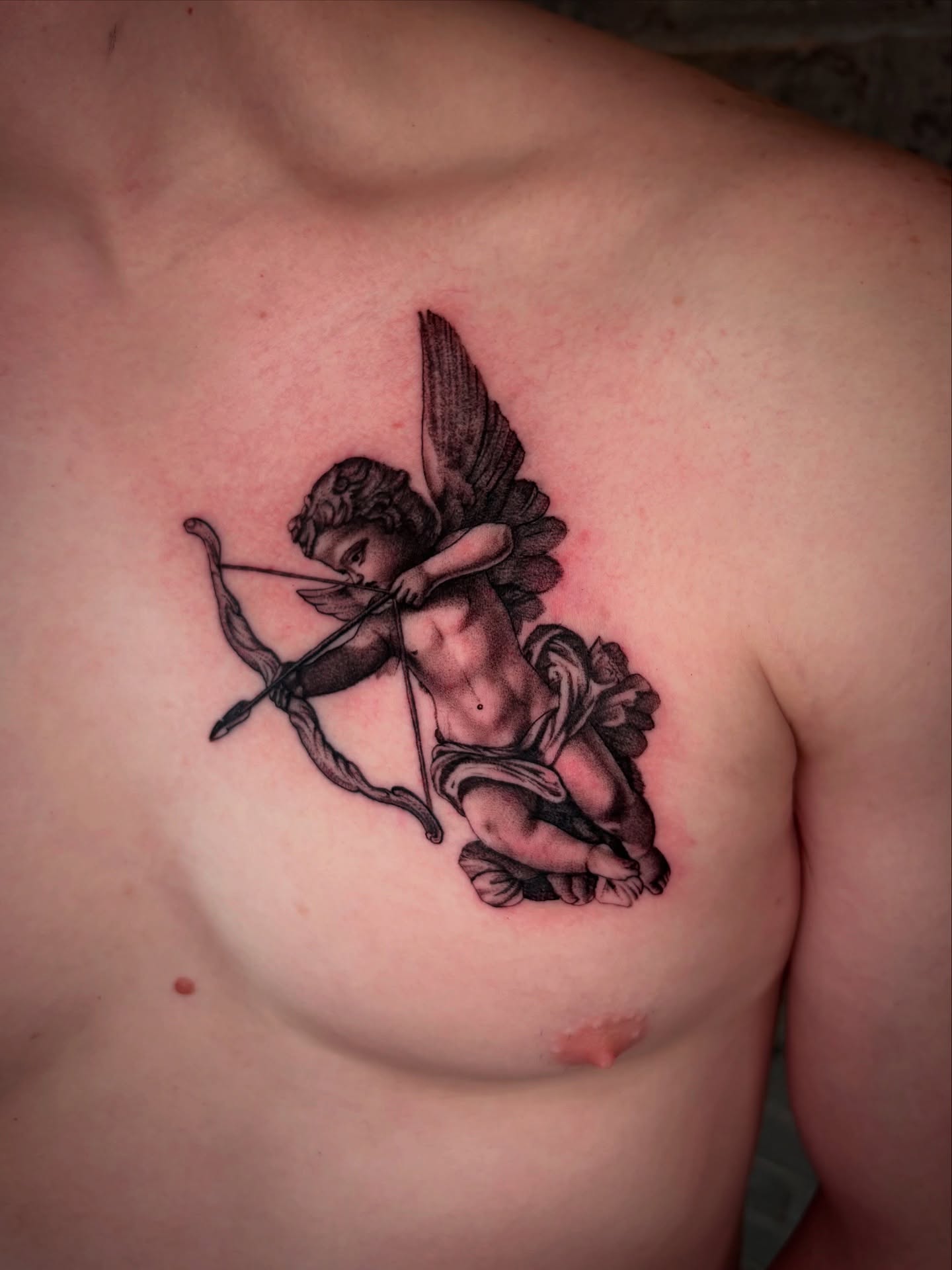 Cherub with bow black and grey tattoo on the chest by JoannaTattoos