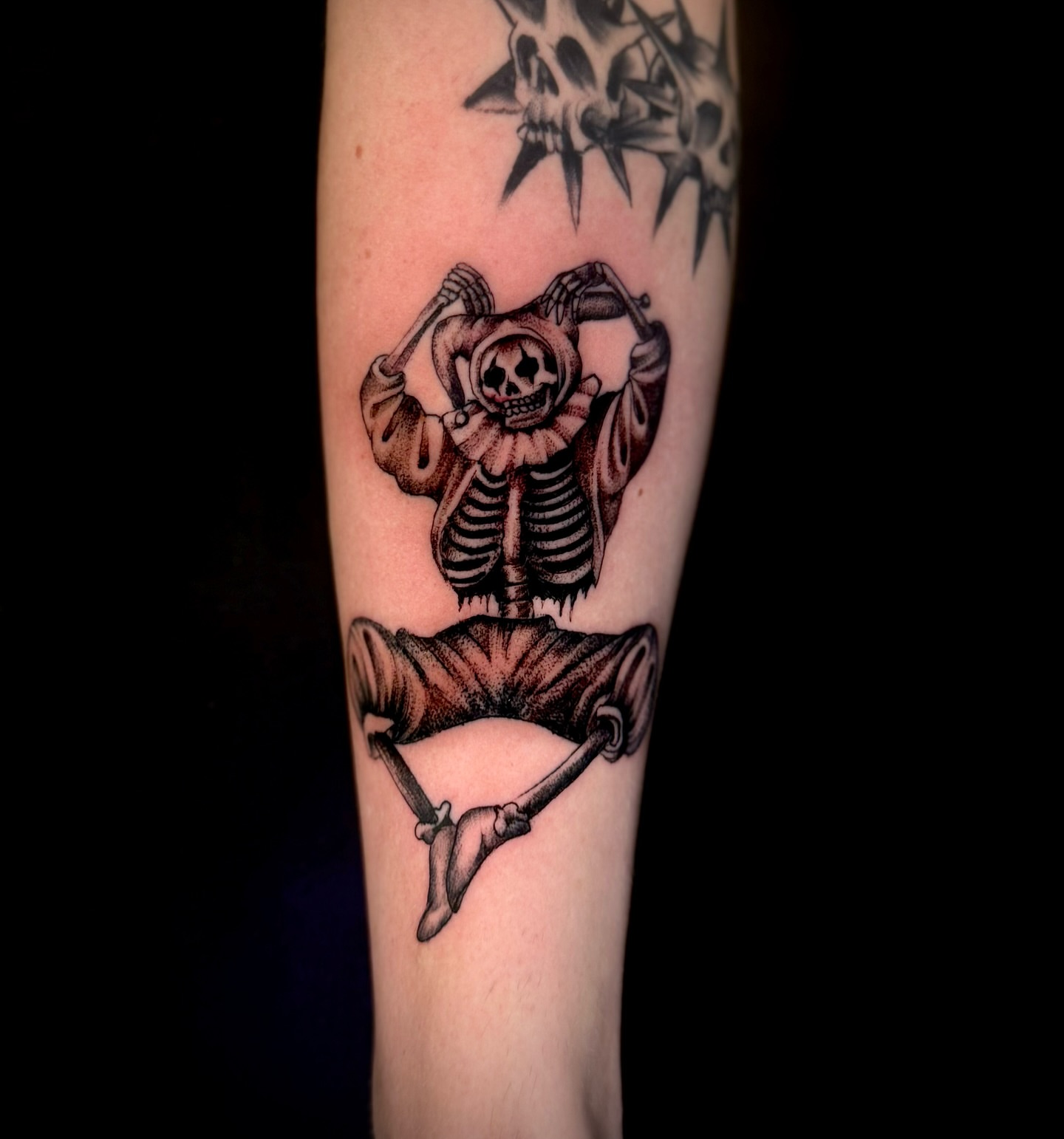 Skeleton in clown costume black and grey tattoo on the forearm by Thomas Martinez