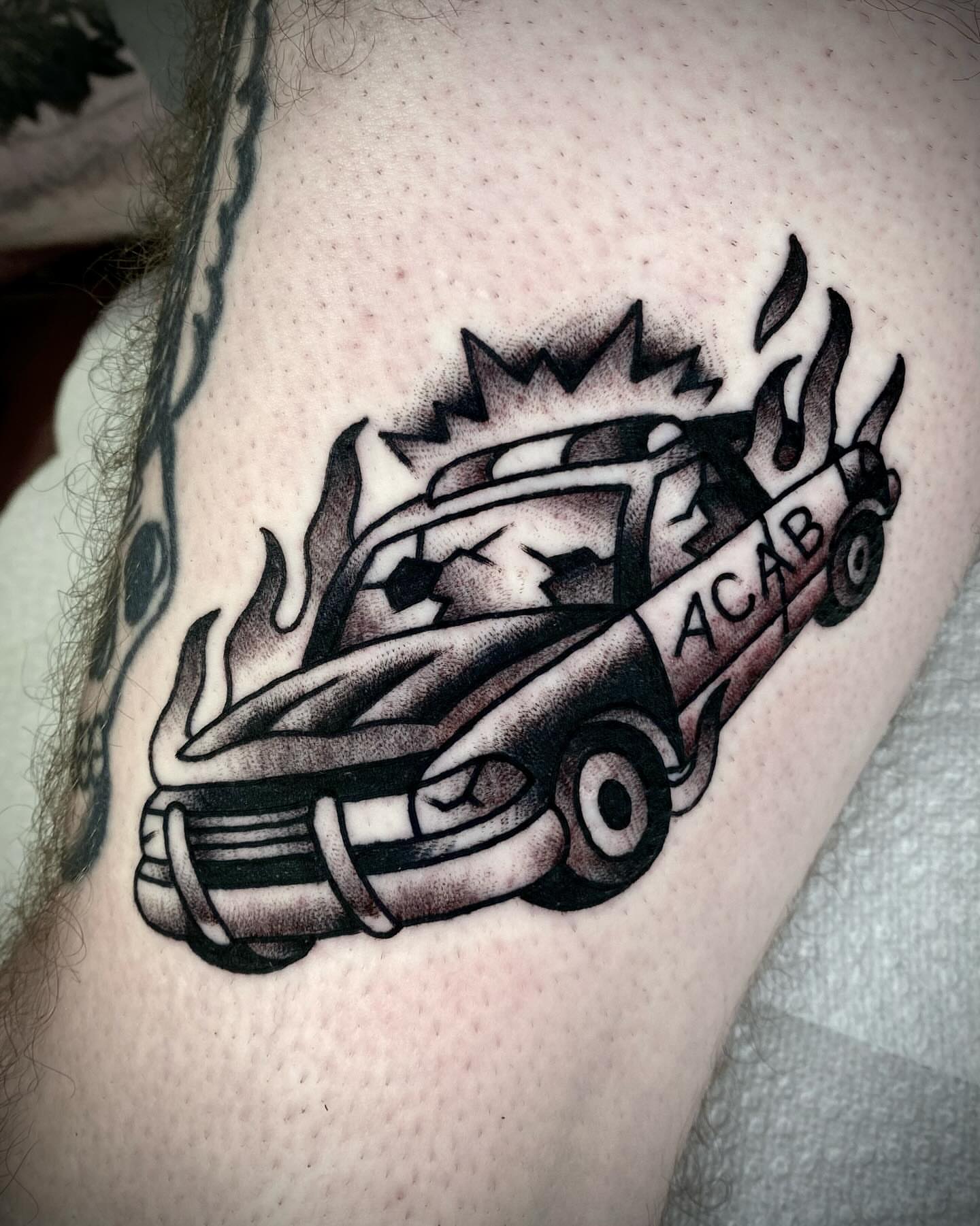 Burning police car American traditional tattoo on the shoulder by Zach Knisley (Wiz)