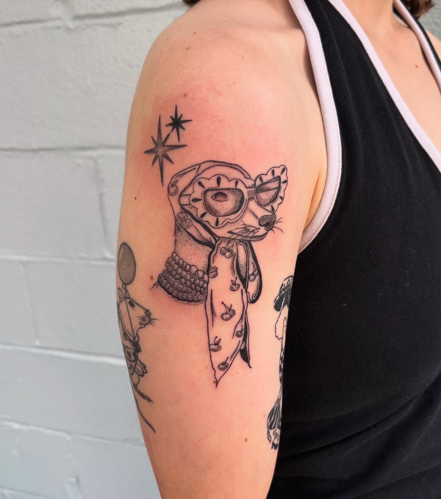 Cat wearing goggles black and grey tattoo on the upper arm by Ashley Ellerman