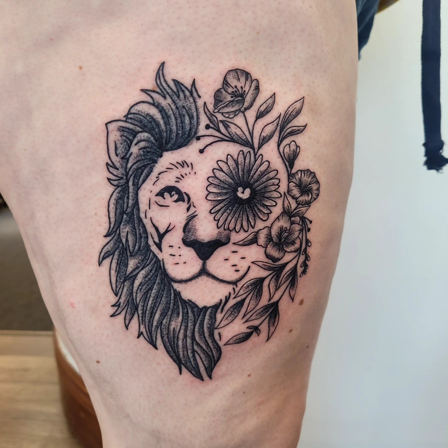Lion with floral elements dotwork tattoo on the thigh by Wray Saulsberry