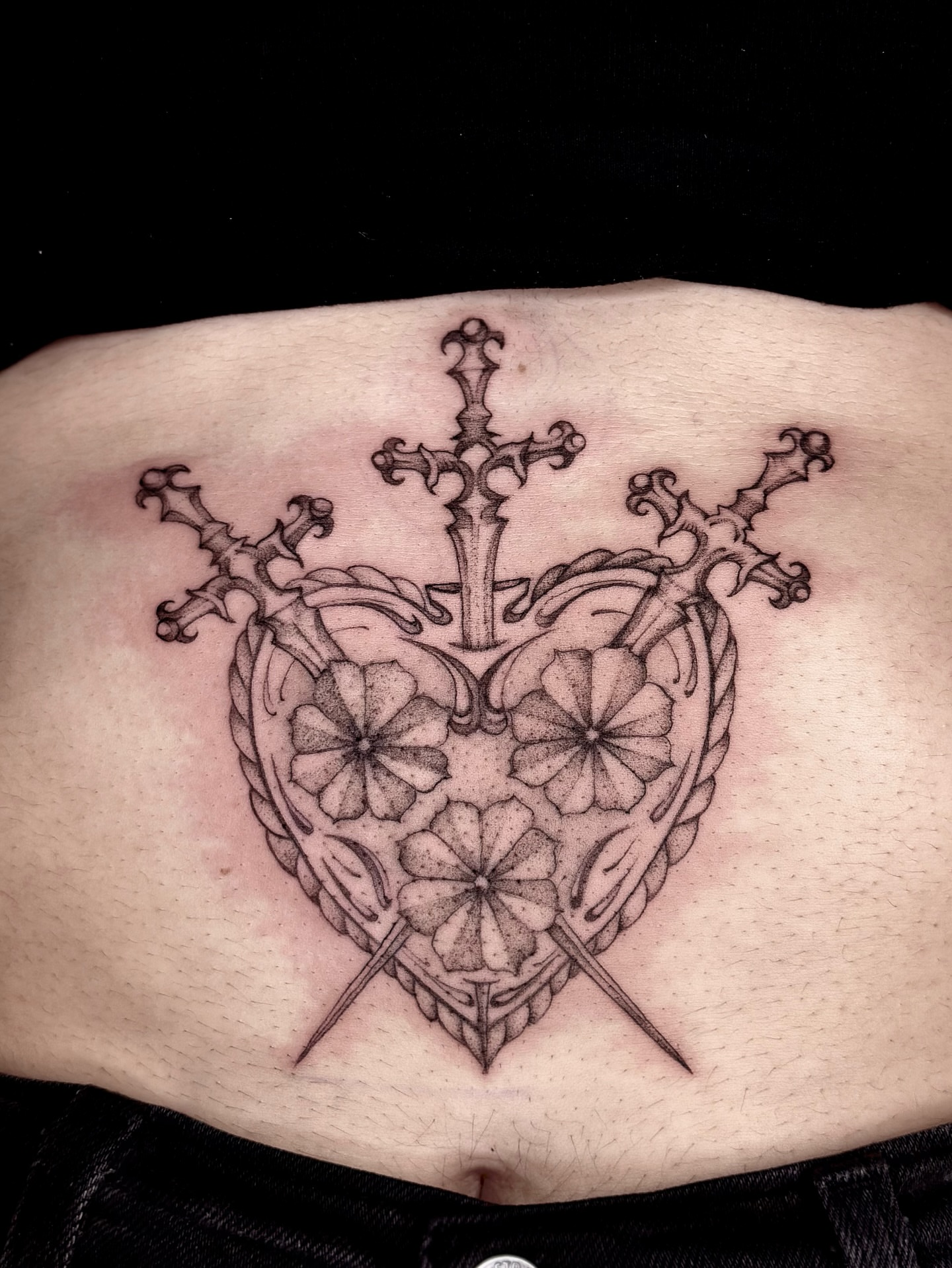 Heart with swords black and grey tattoo on the ribs by cora cupid