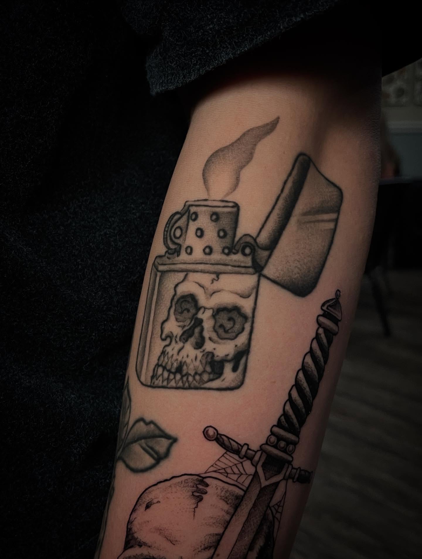 Lighter with skull black and grey tattoo on the forearm by Caleb Baker
