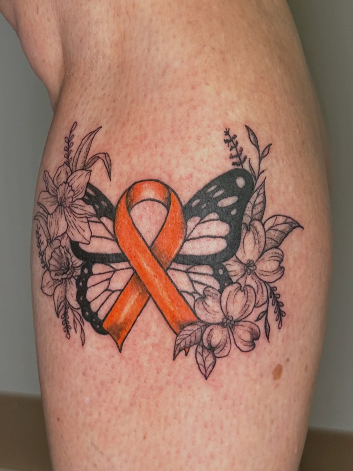Orange ribbon with butterfly and flowers black and grey tattoo on the thigh by B A B y
