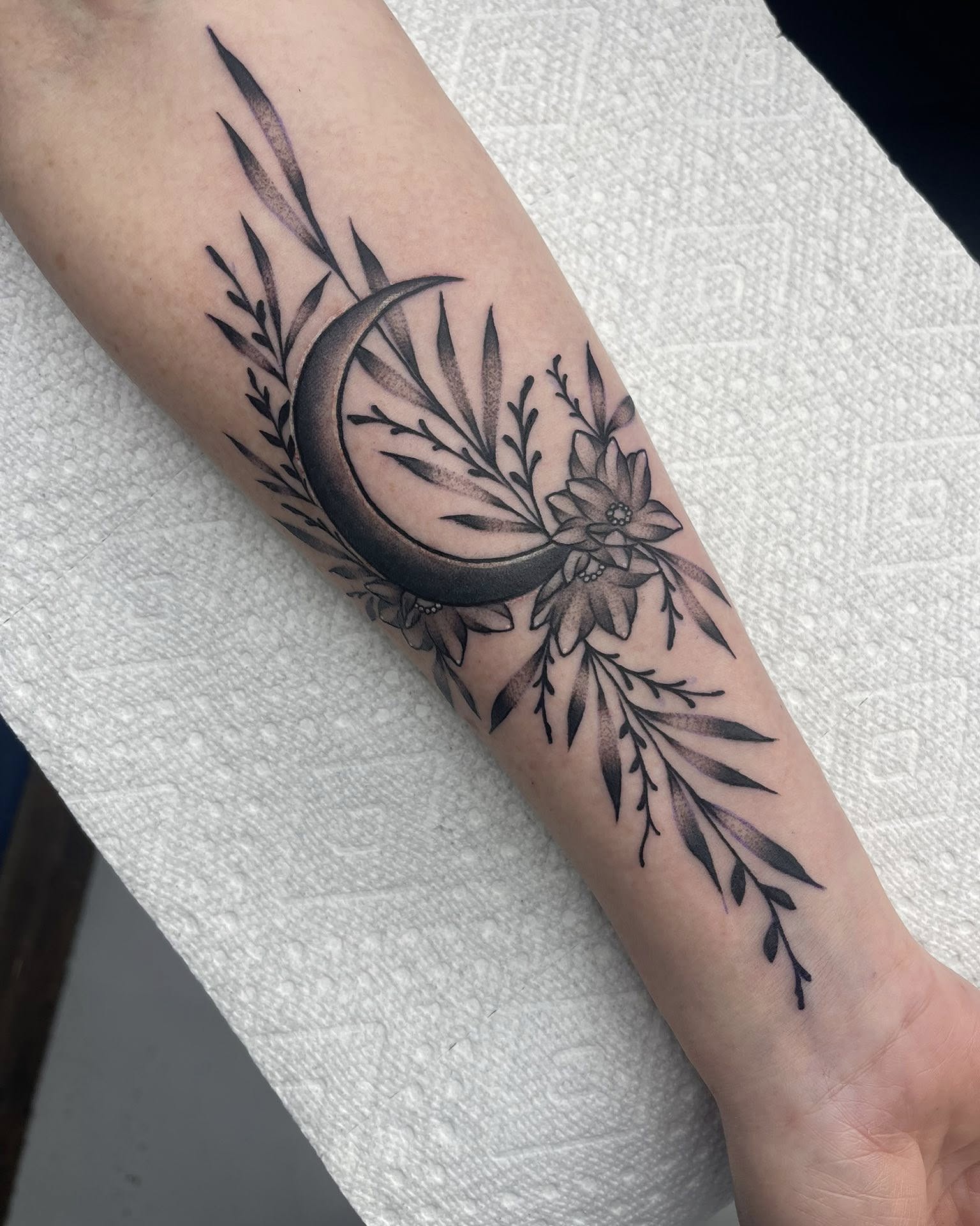 Moon and floral arrangement fine line tattoo on the forearm by Autumn Fulford