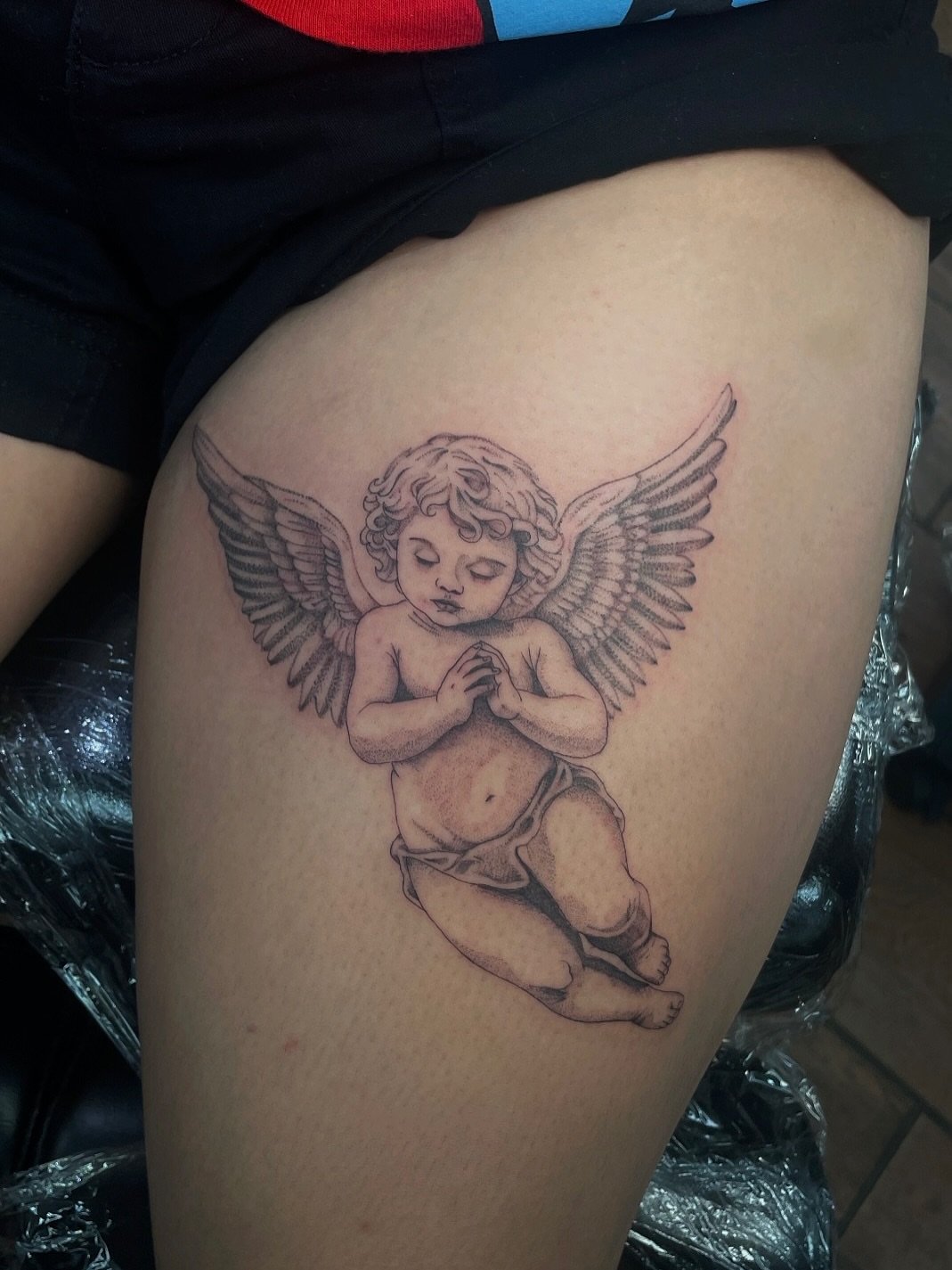 Cherub black and grey tattoo on the thigh by 𝕯𝖔𝖒