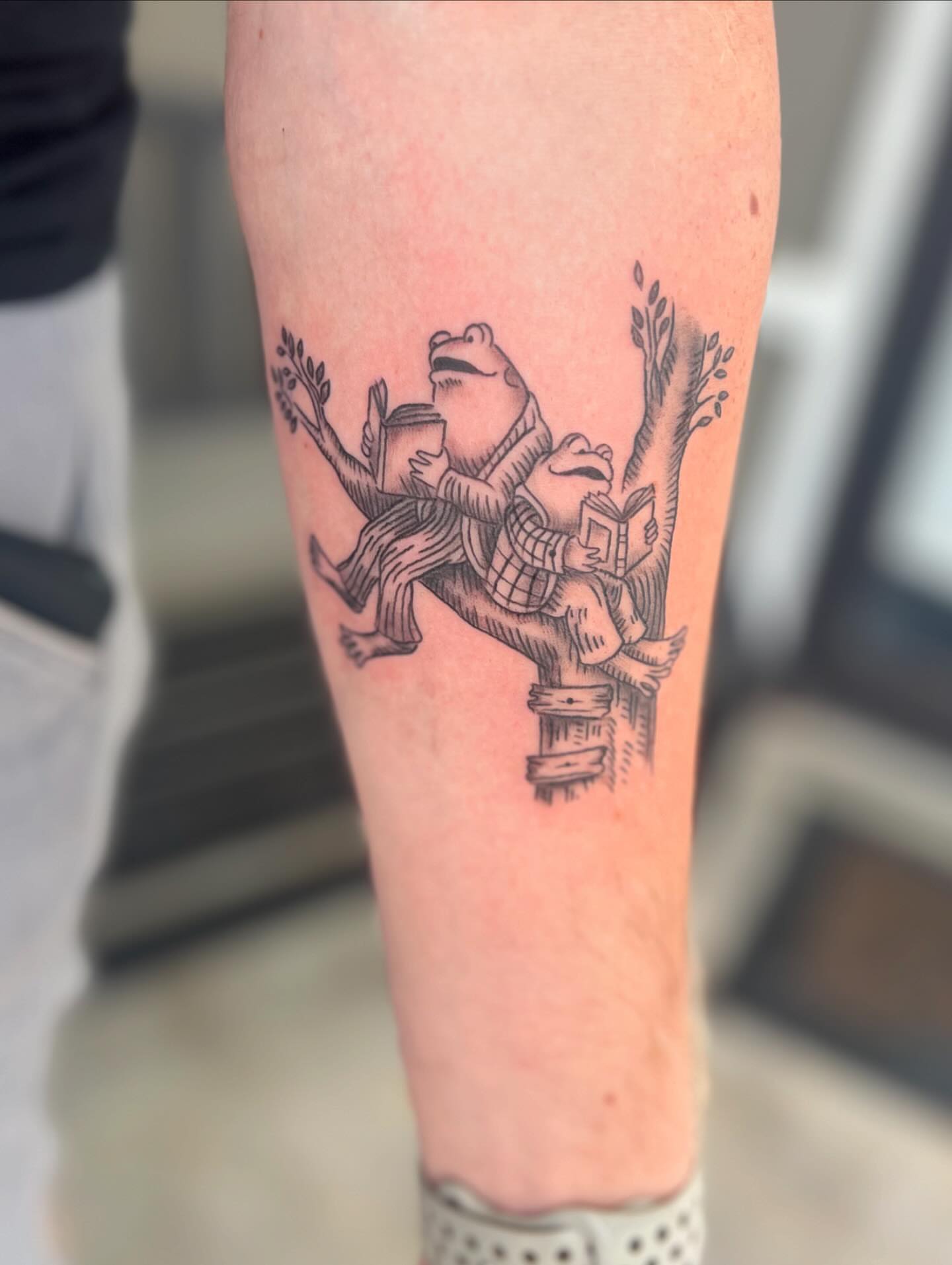 Frogs reading books black and grey tattoo on the forearm by Jai Woods