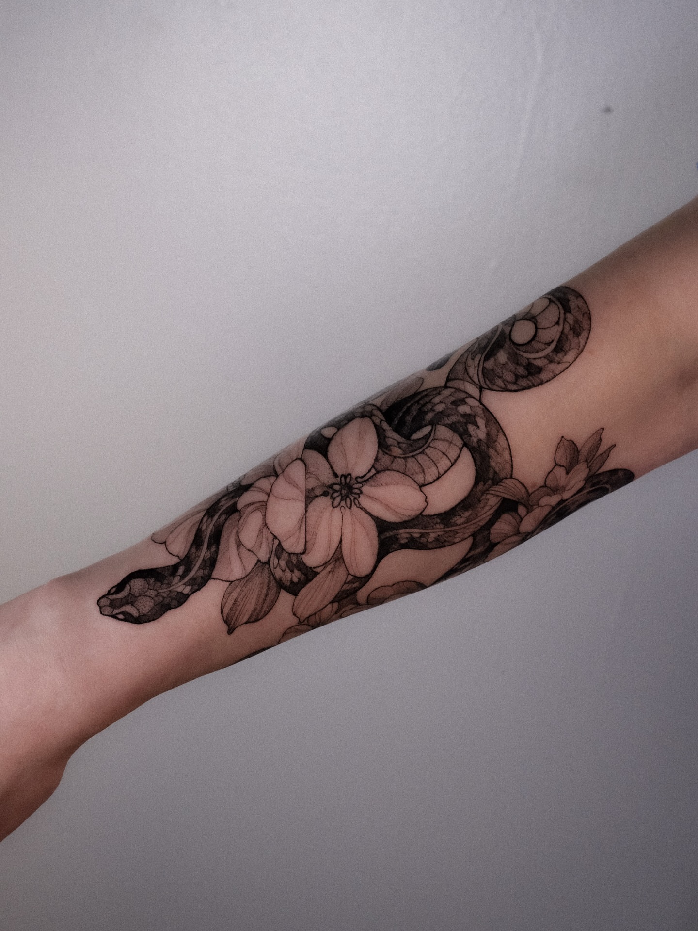 Snake and flowers black and grey tattoo on the forearm by Alena Zozulenko