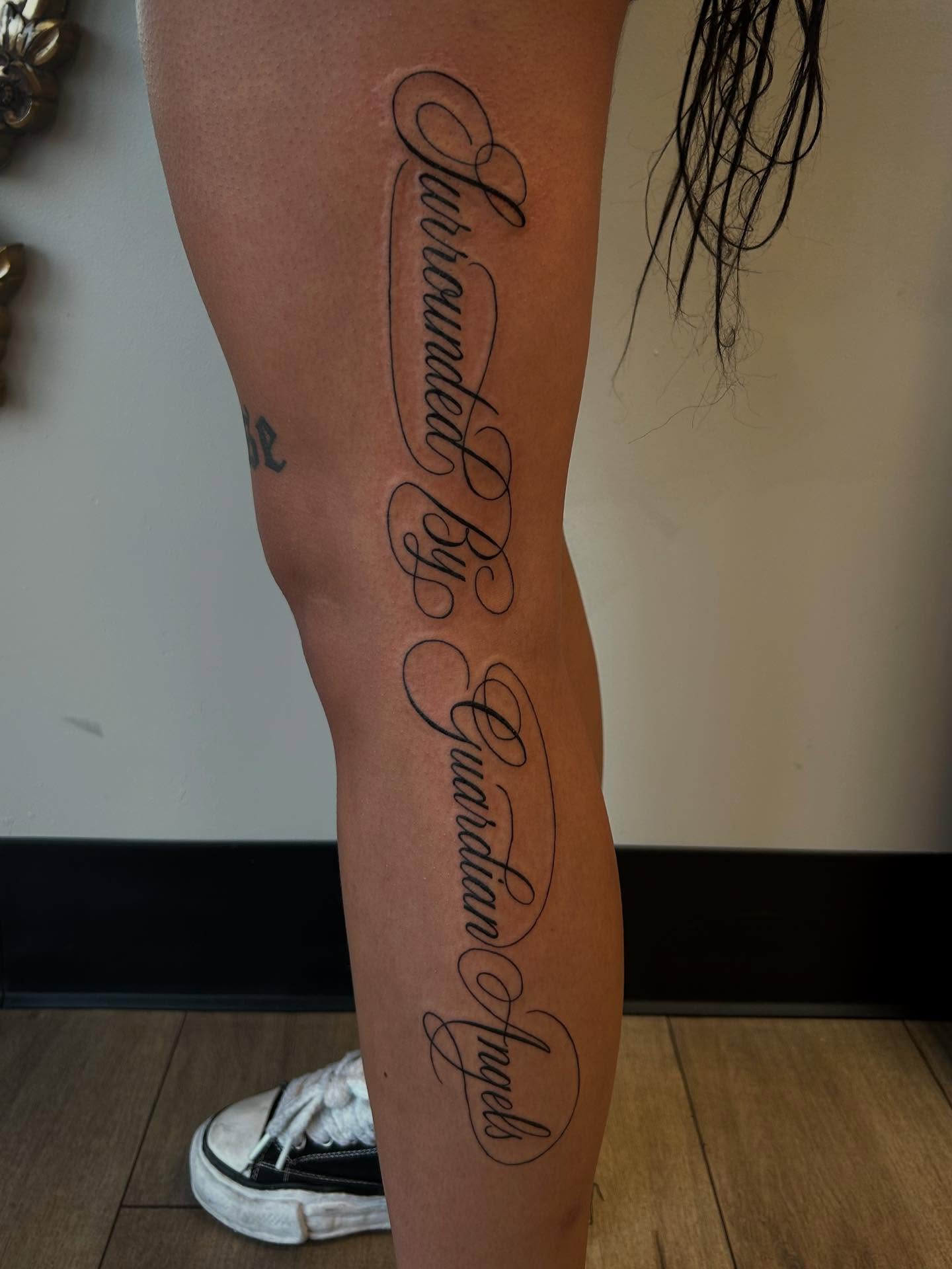 Surrounded by guardian angels lettering script tattoo on the calf by 𝕯𝖆𝖓𝖎