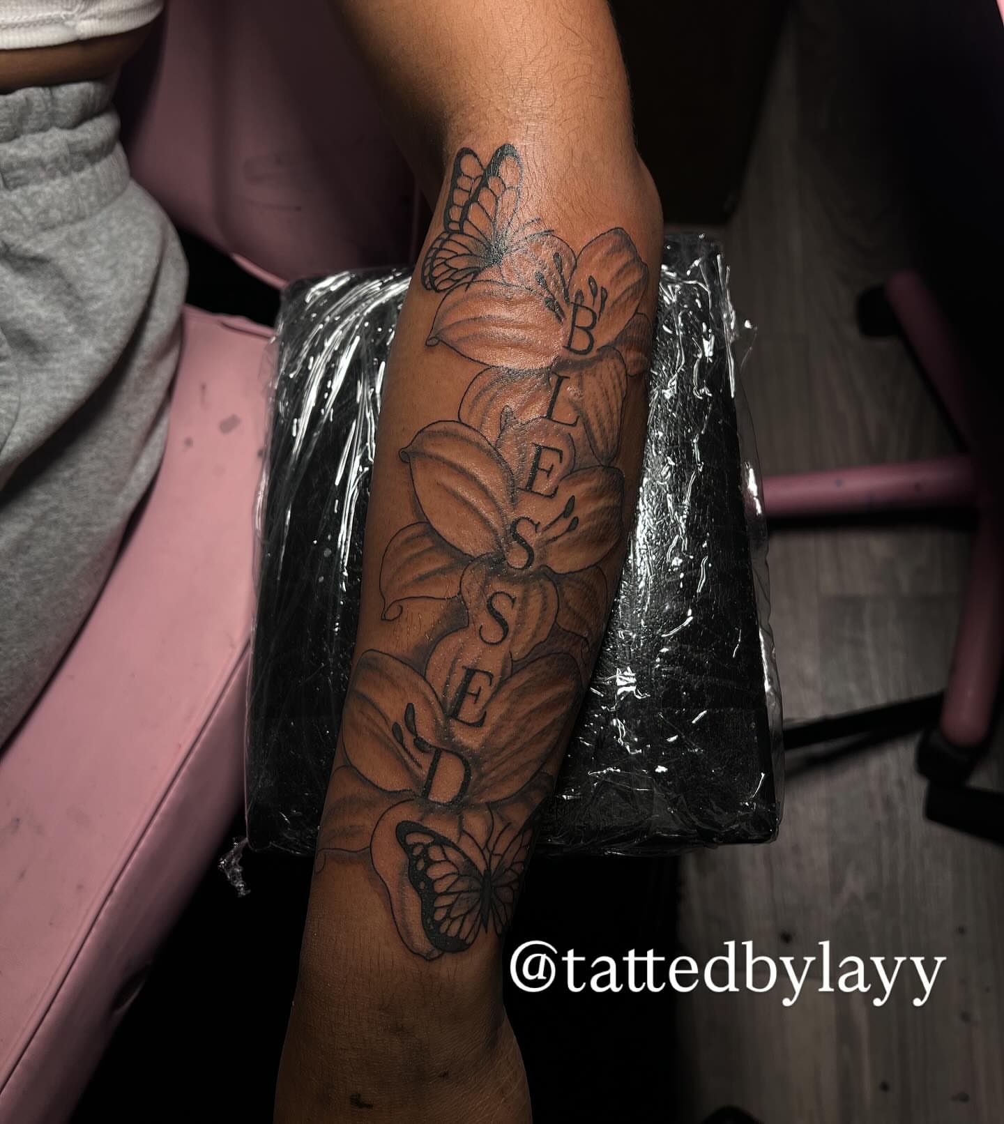 Flowers and butterflies black and grey tattoo on the forearm by Tatted By Layy