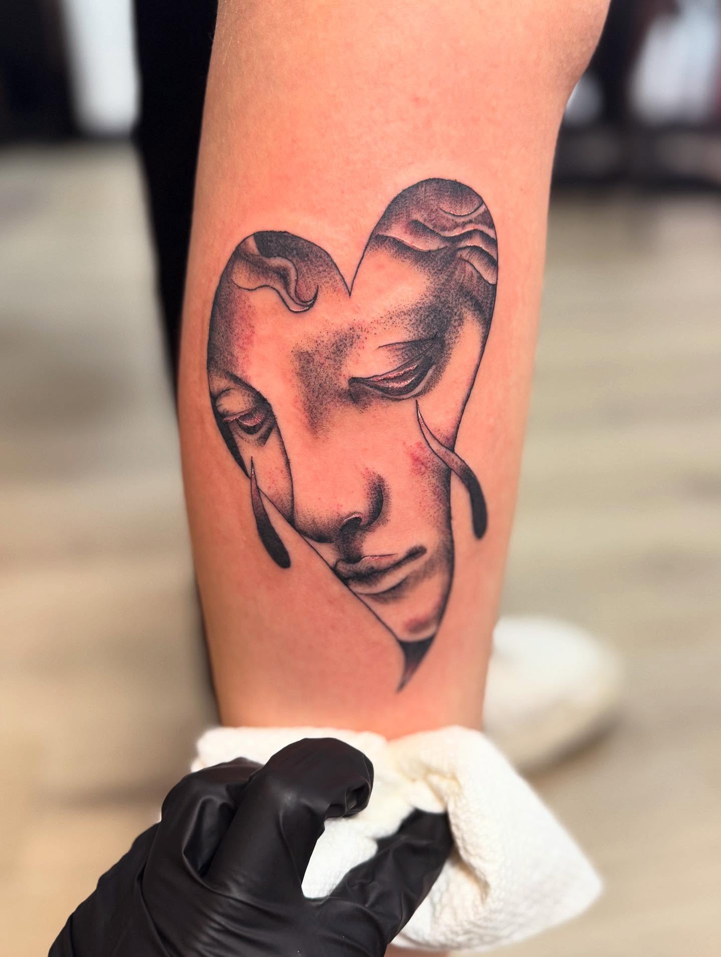 Heart-shaped face black and grey tattoo on the forearm by Cohen
