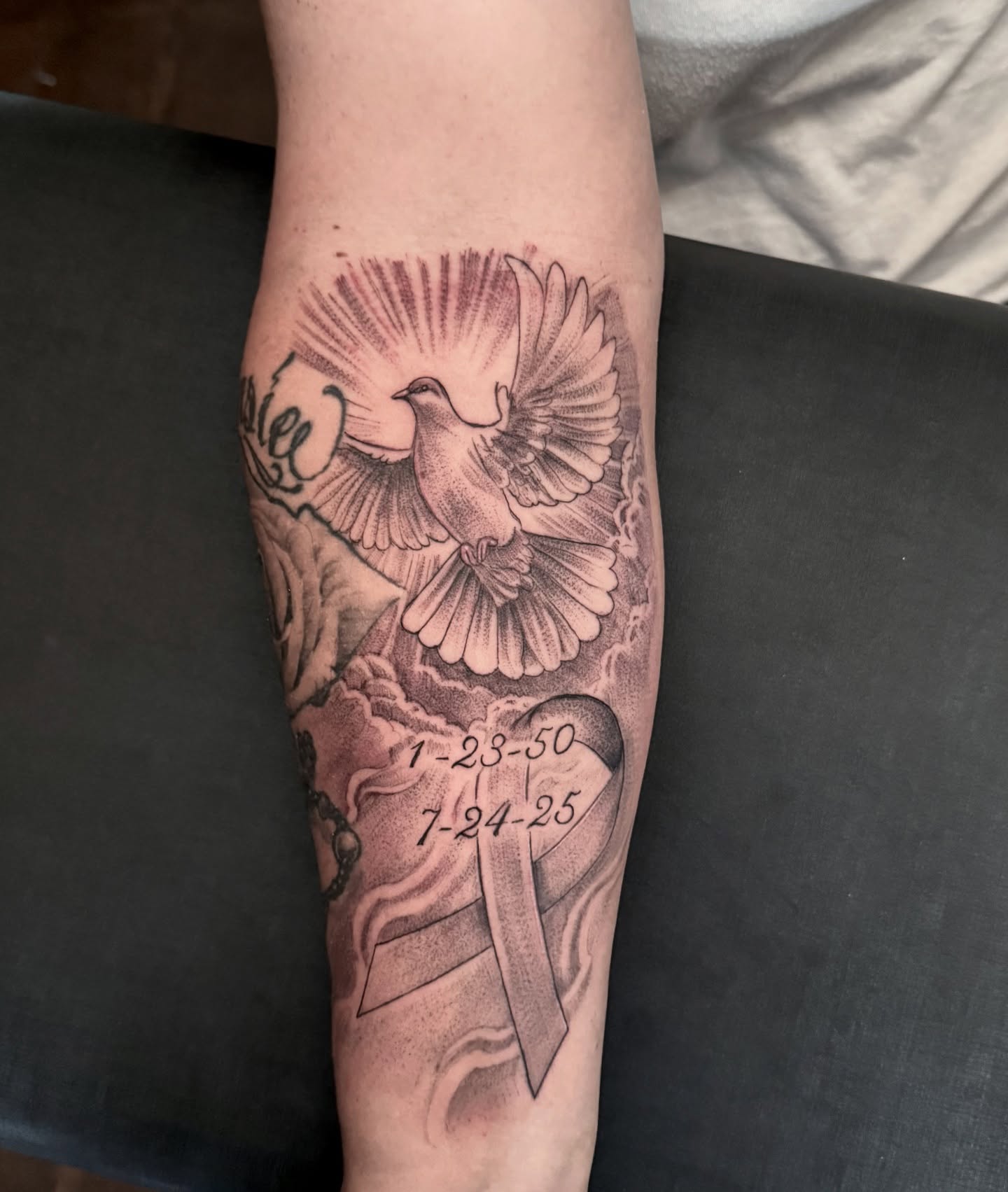 Dove and ribbon black and grey tattoo on the forearm by Tattoo Artist