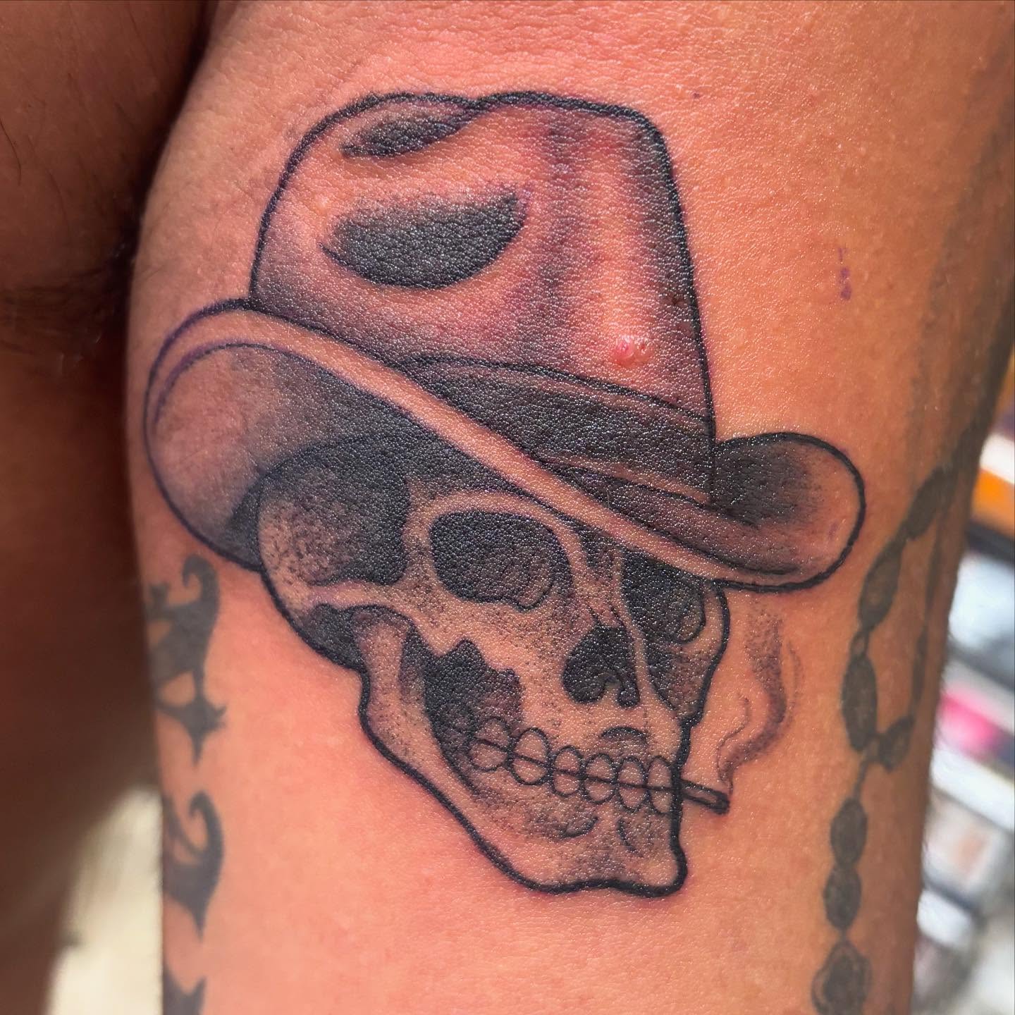 Skull wearing hat black and grey tattoo on the forearm by Oscar Cuéllar (Kue-Yar)