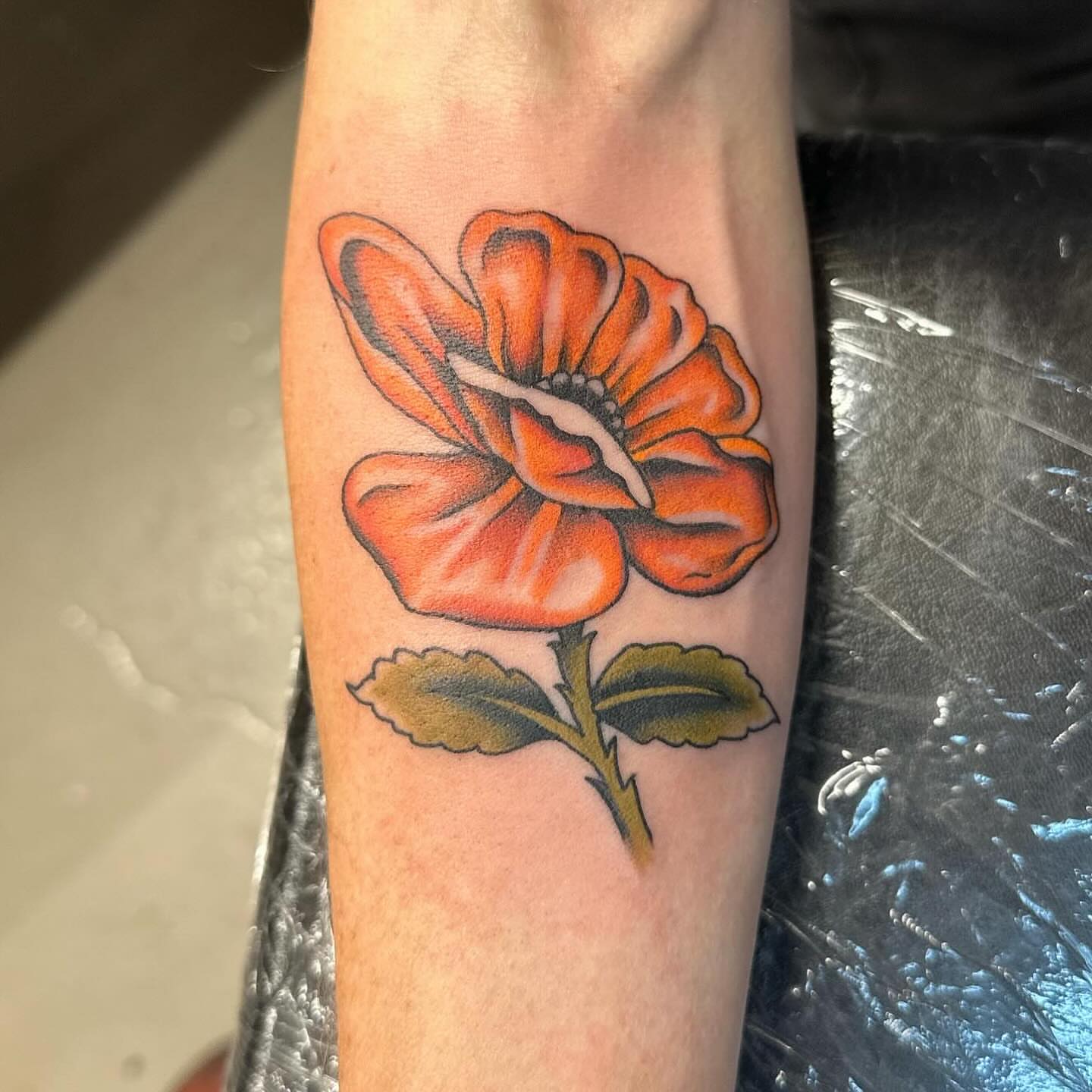 Orange flower realism tattoo on the forearm by Stacy Fevinger