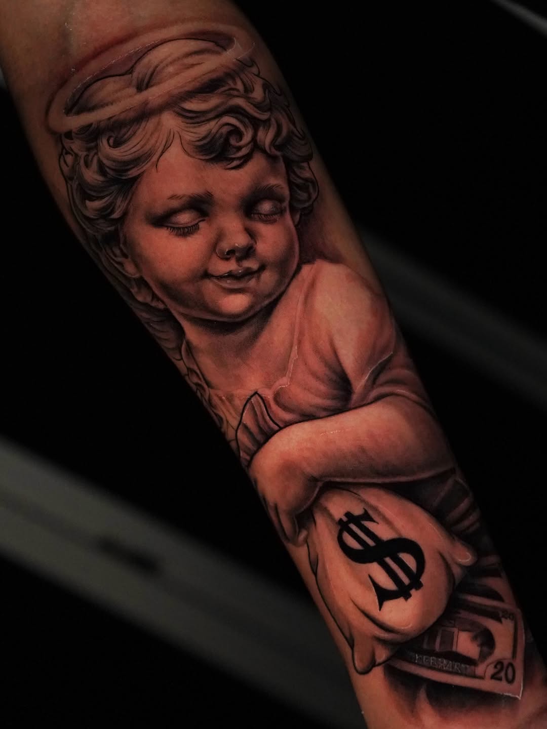 Cherub holding money bag realism tattoo on the forearm by Jennifer Garcia