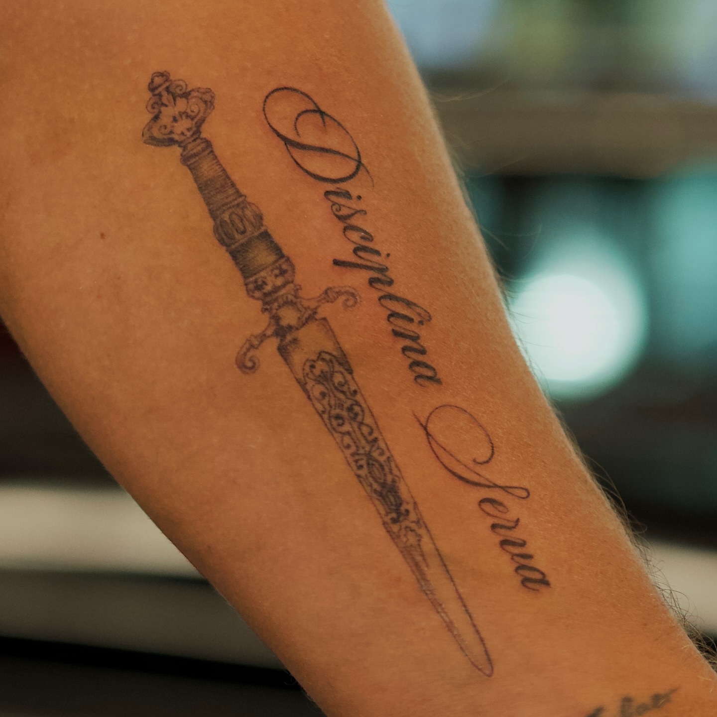 Sword and cursive text black and grey tattoo on the forearm by @blackastaratattoo