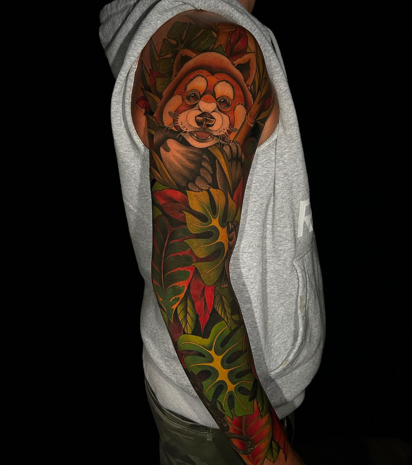 Red panda in jungle realism tattoo on the upper arm by Lexi Kniskern