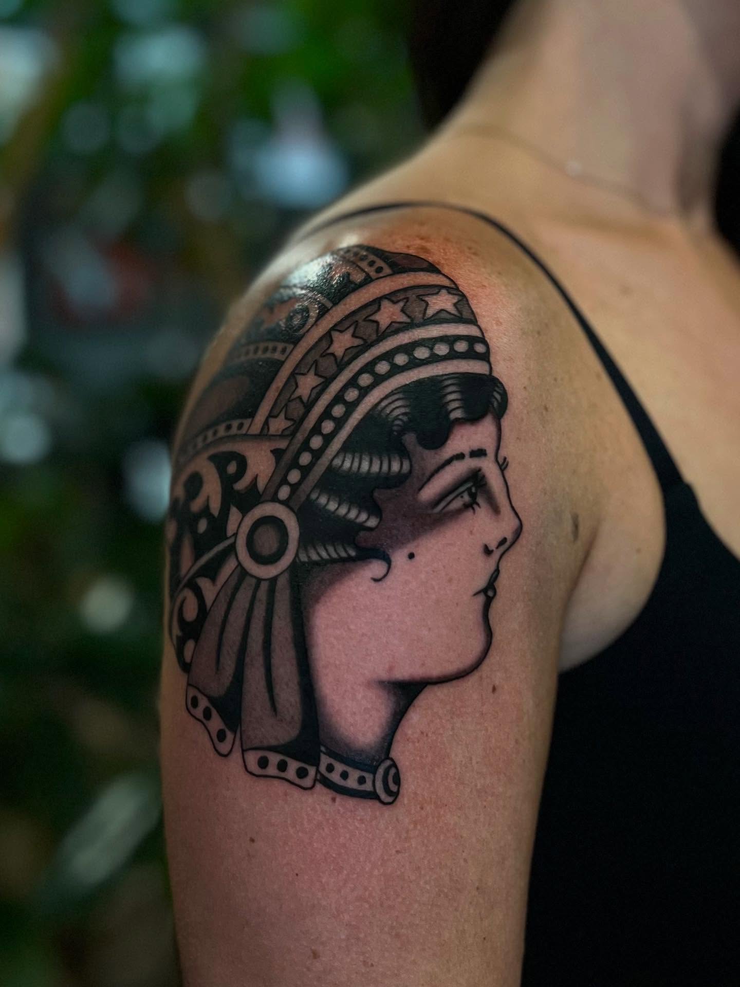 Woman with headdress black and grey tattoo on the shoulder by Syd Sayyah