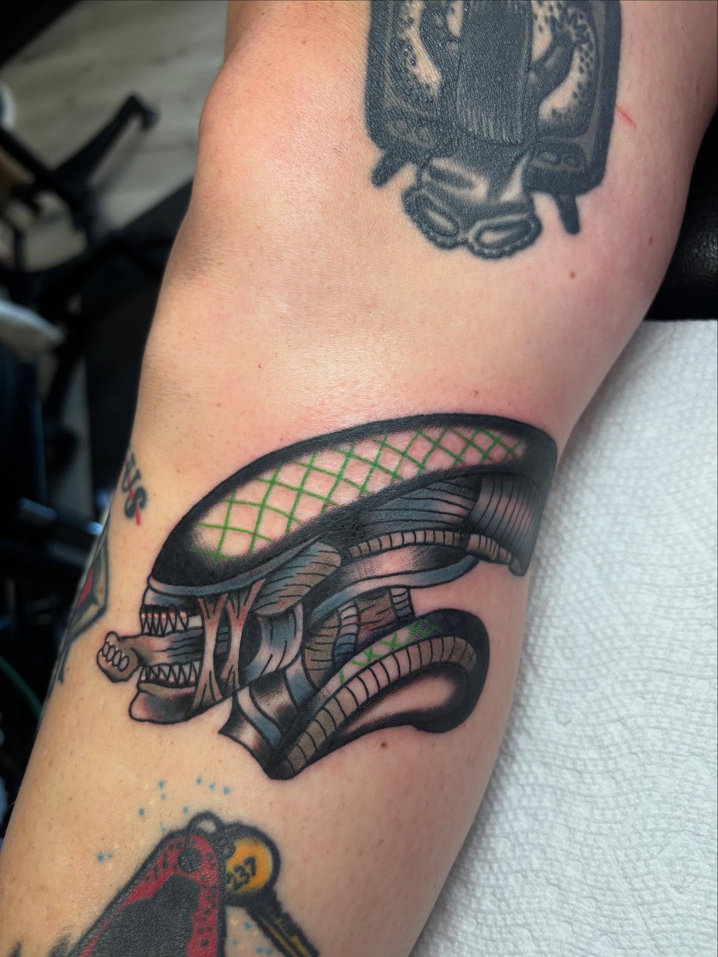 Alien head black and grey tattoo on the forearm by Ben Whyte