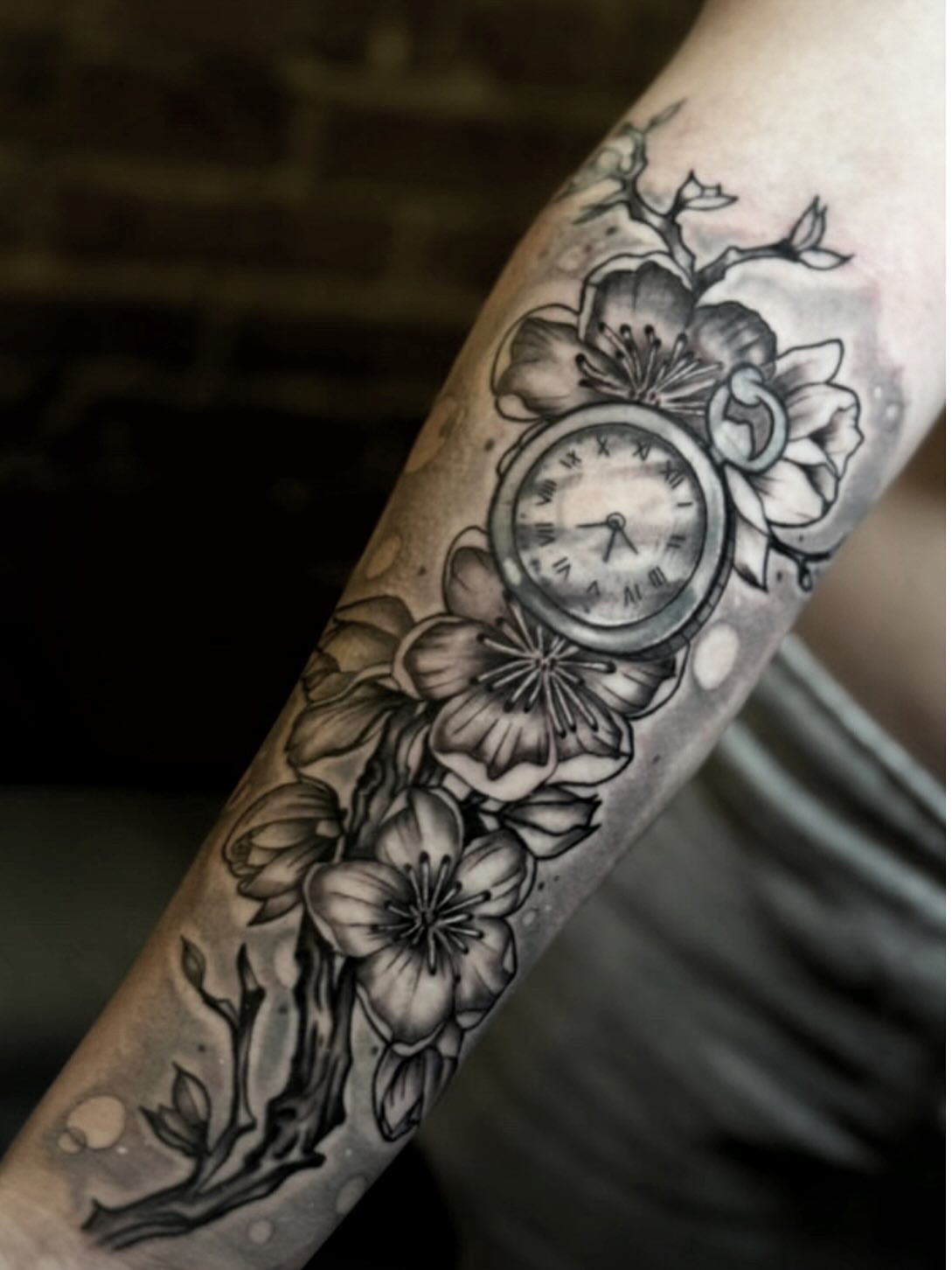 Clock with floral elements black and grey tattoo on the forearm by Shake_tatts