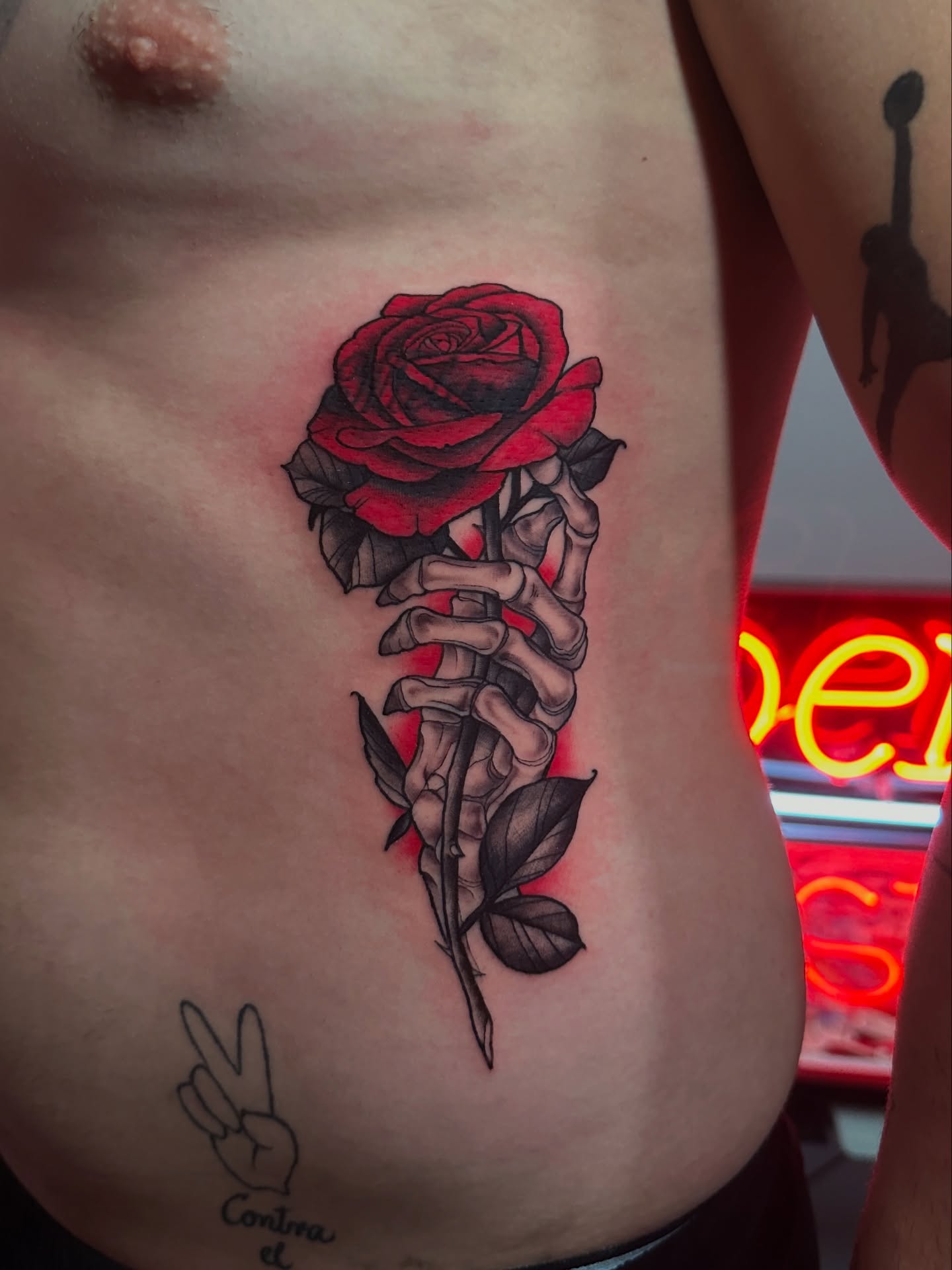 Red rose with skeleton hand realism tattoo on the ribs by Dennis Alejandro
