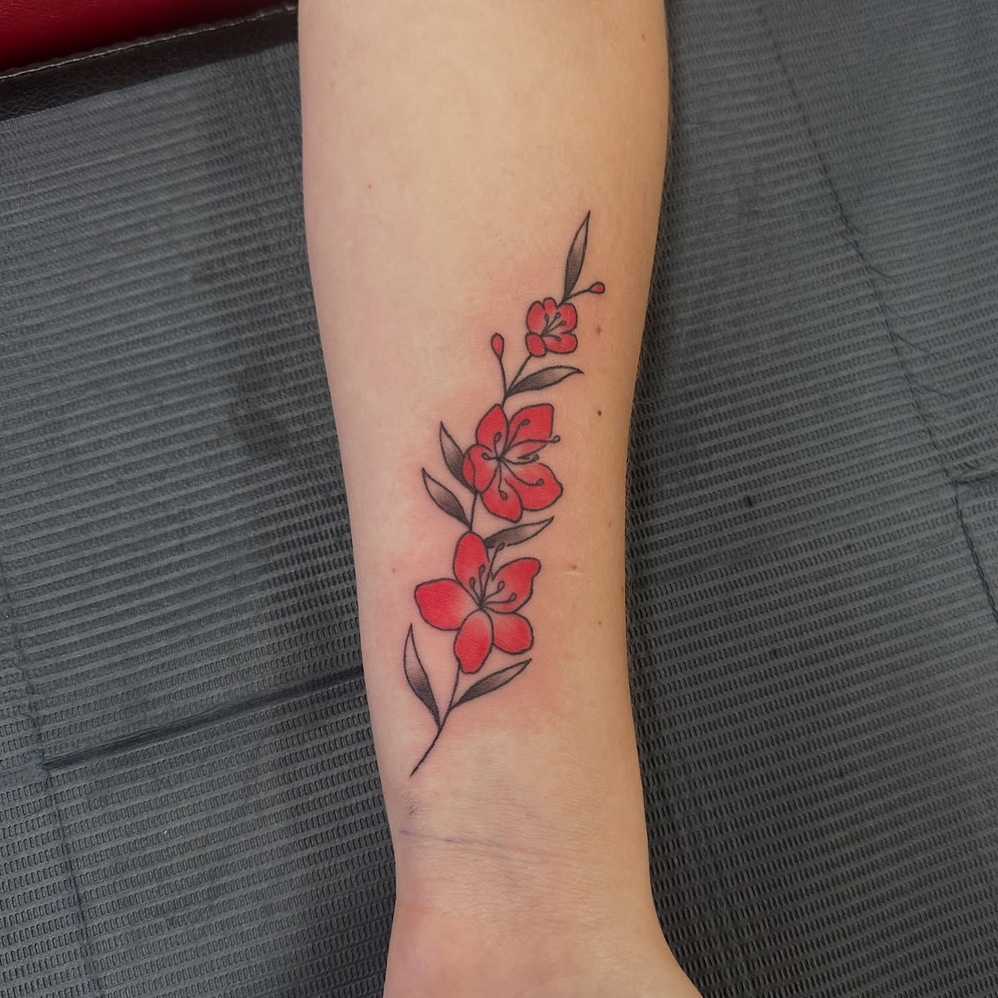 Red flowers new school tattoo on the forearm by Bosco Layne