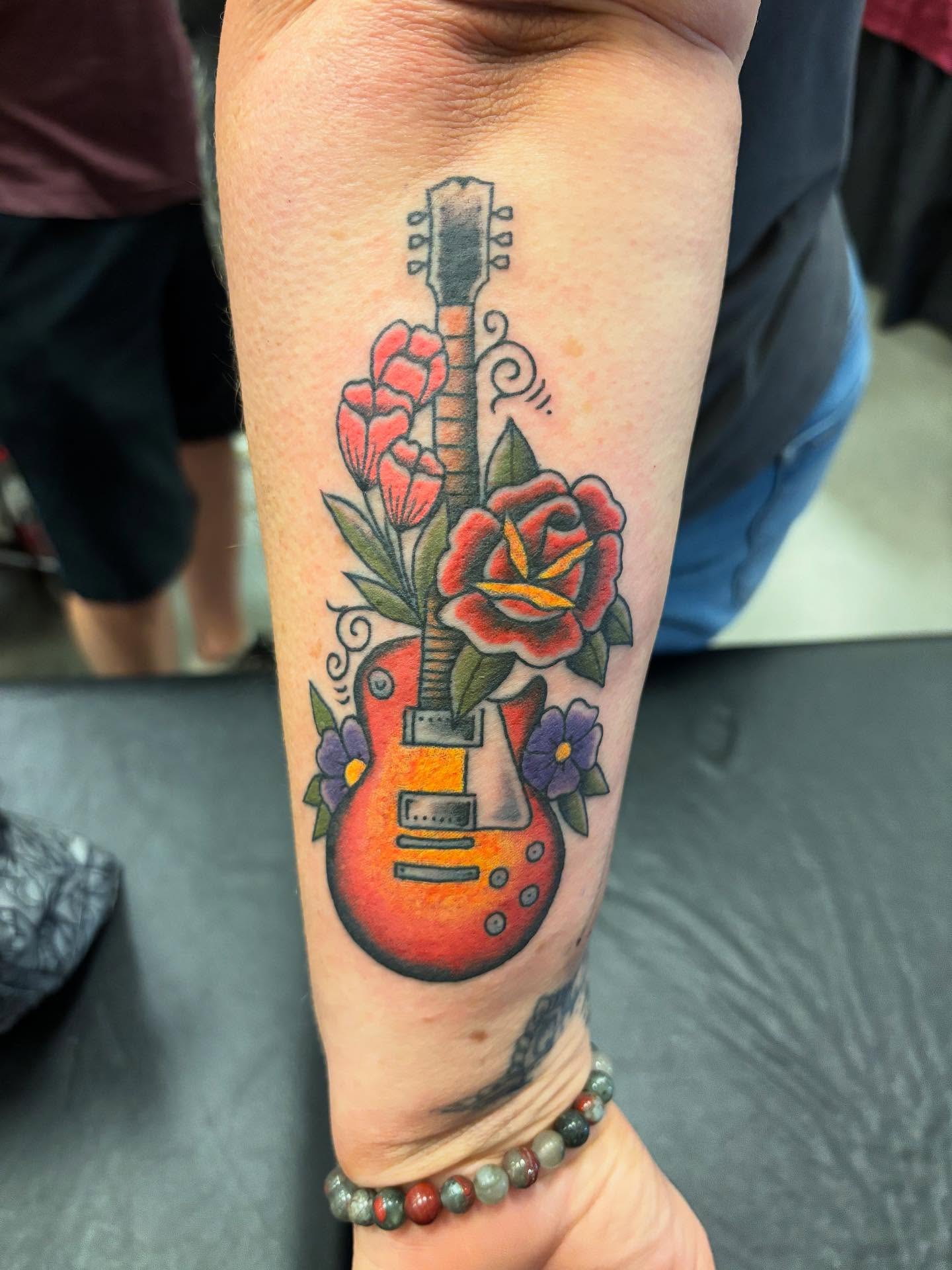 Electric guitar with flowers American traditional tattoo on the forearm by Angie Isbell