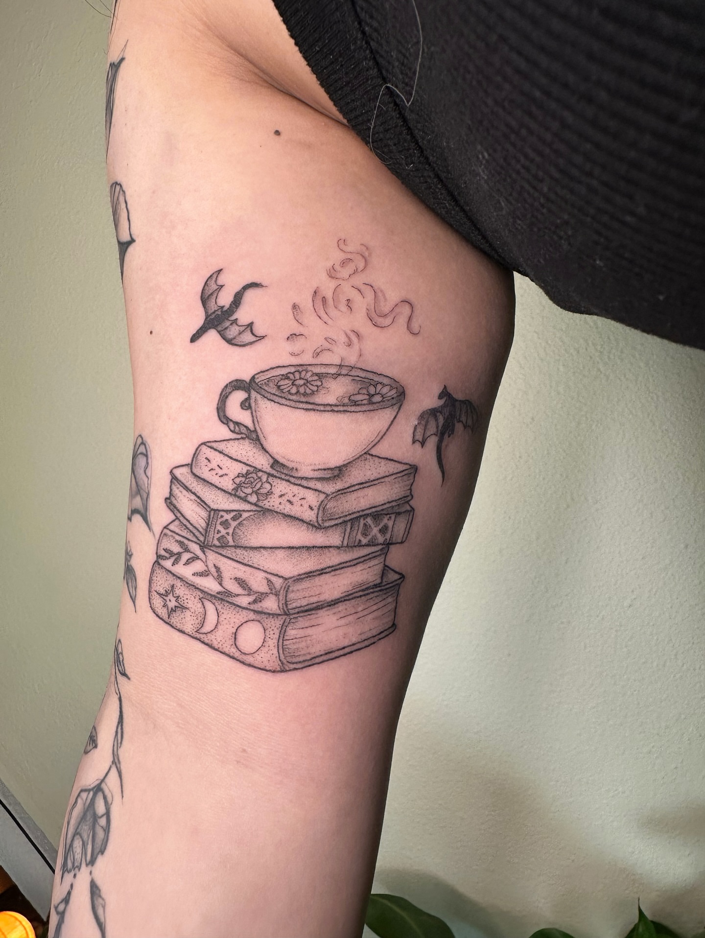Stack of books with coffee cup black and grey tattoo on the forearm by kenzie hunter