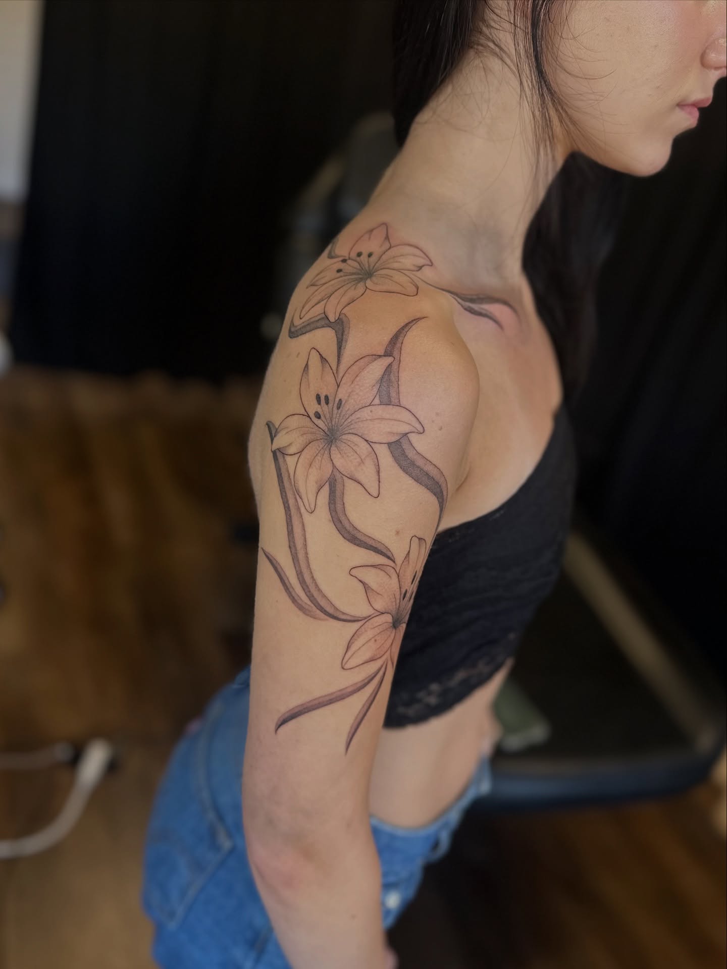 Lilies black and grey tattoo on the upper arm by Priscilla Michels