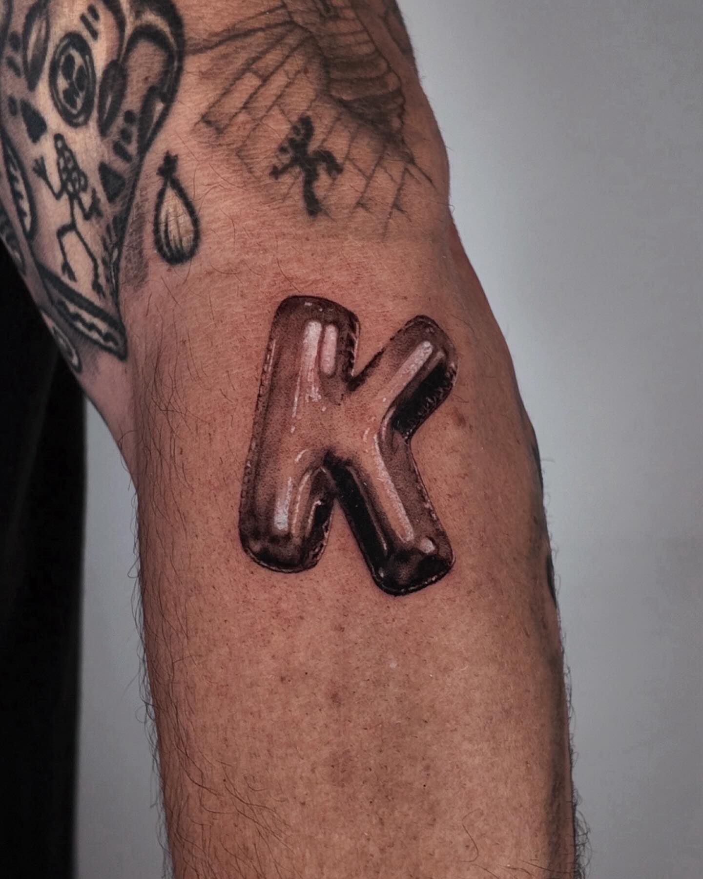 Letter K black and grey tattoo on the forearm by Gabriel