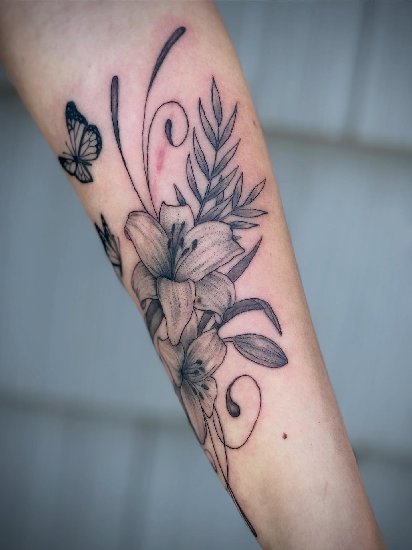Lilies and butterfly black and grey tattoo on the forearm by Iconic Ink, Millbury, Massachusetts