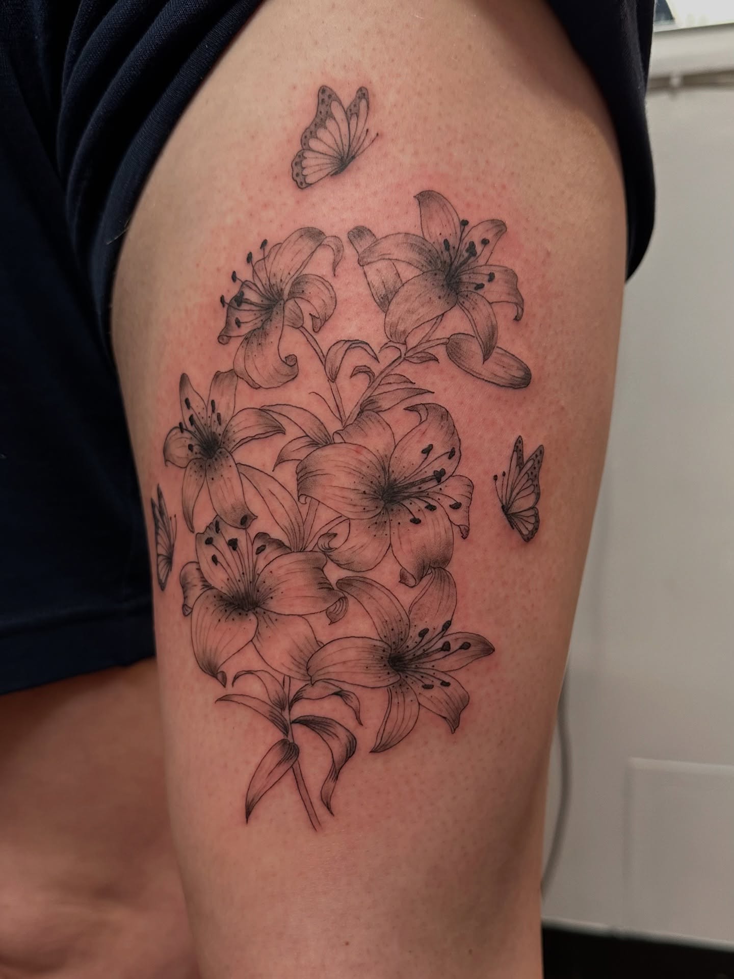 Lilies and butterflies black and grey tattoo on the thigh by Piccolino, Cambridge, Massachusetts
